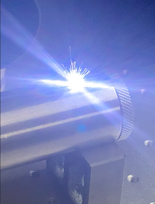 Close-up of an engraving process with bright sparks and blue light emitted from the laser contact on a metal piece.