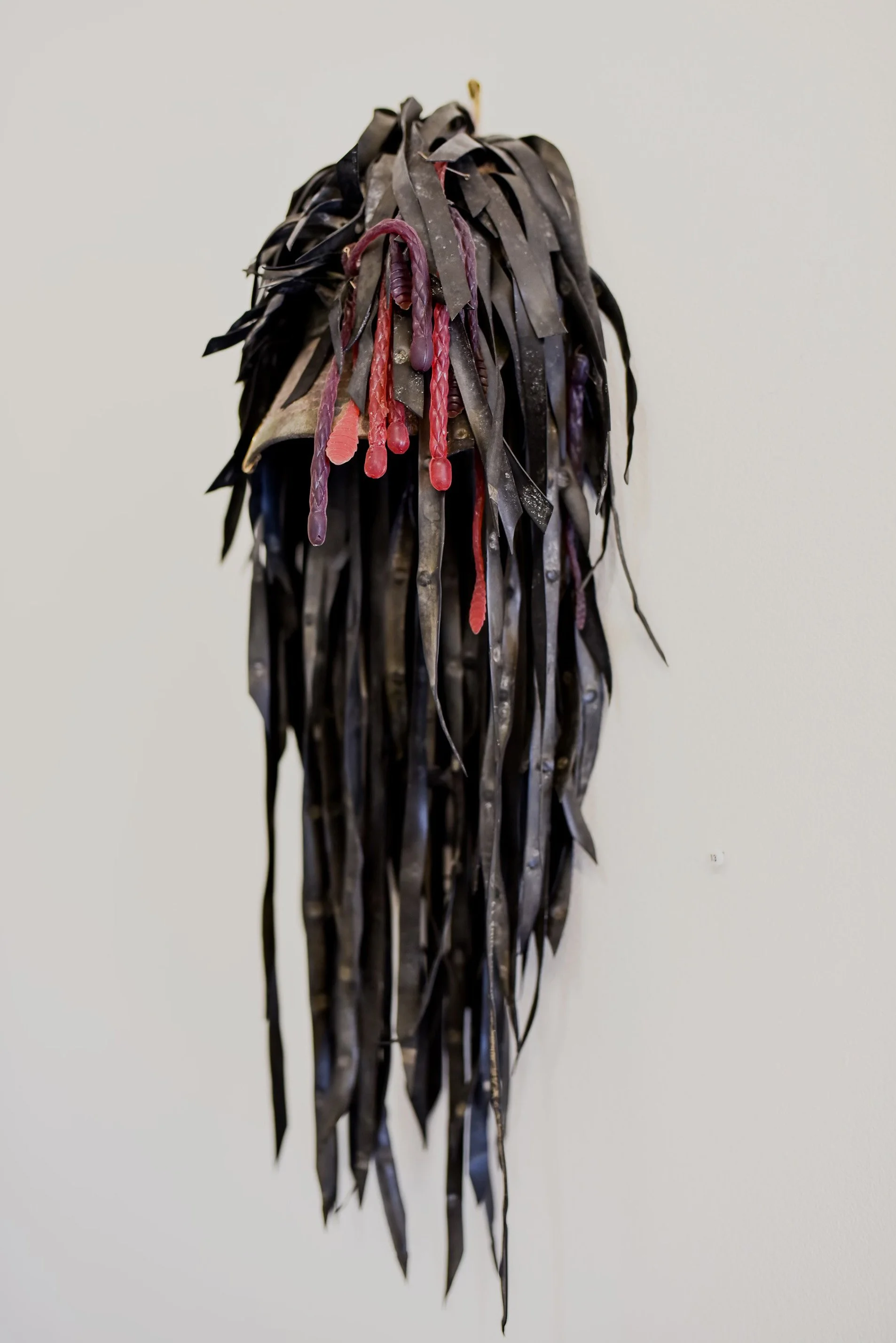 Abstract art piece with black and red ribbon-like materials hanging from a wall