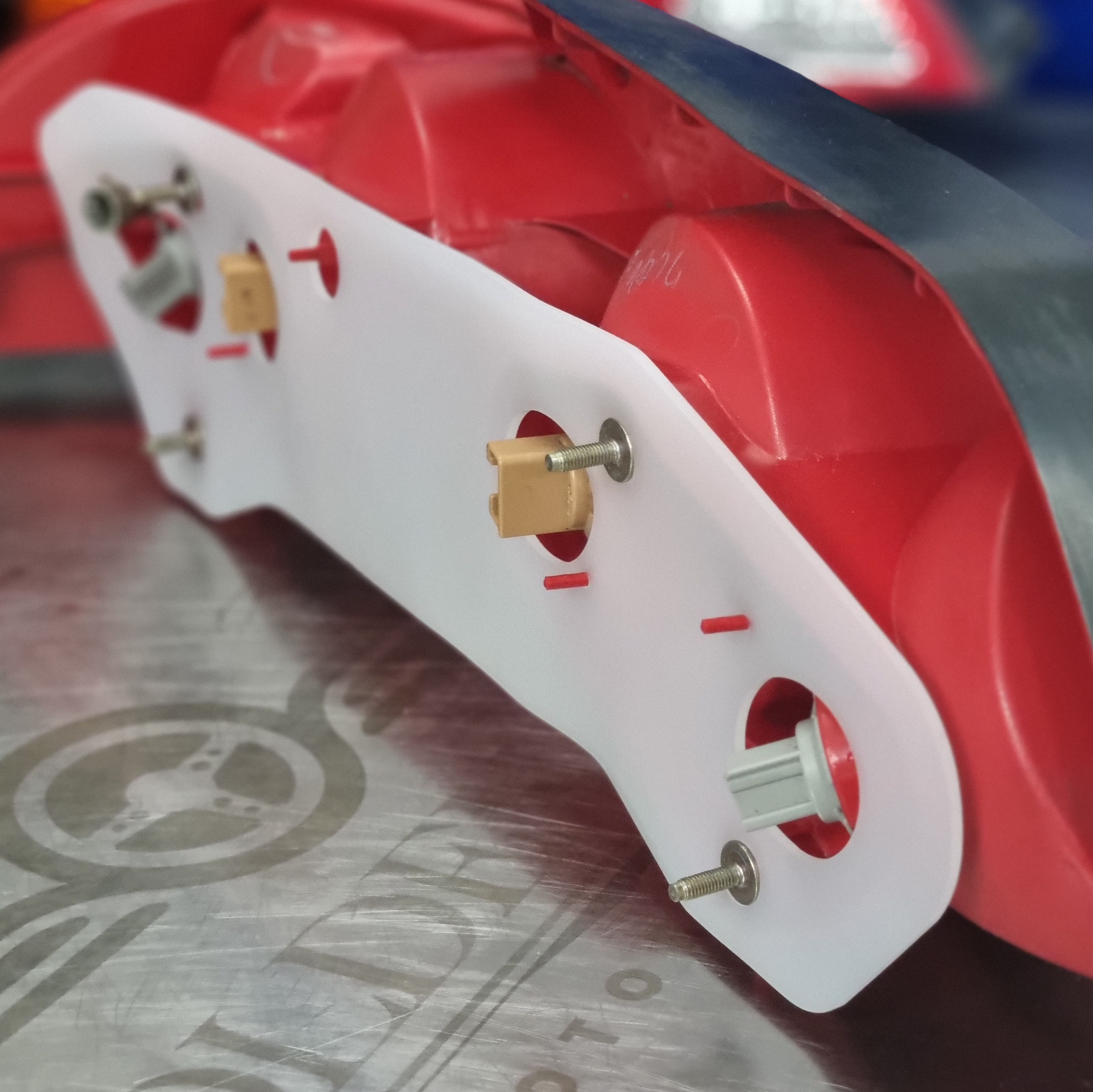 Close-up of a red and white device with metallic screws and small beige plastic parts, possibly machinery or electronic equipment, on a gray surface with a swirl pattern.