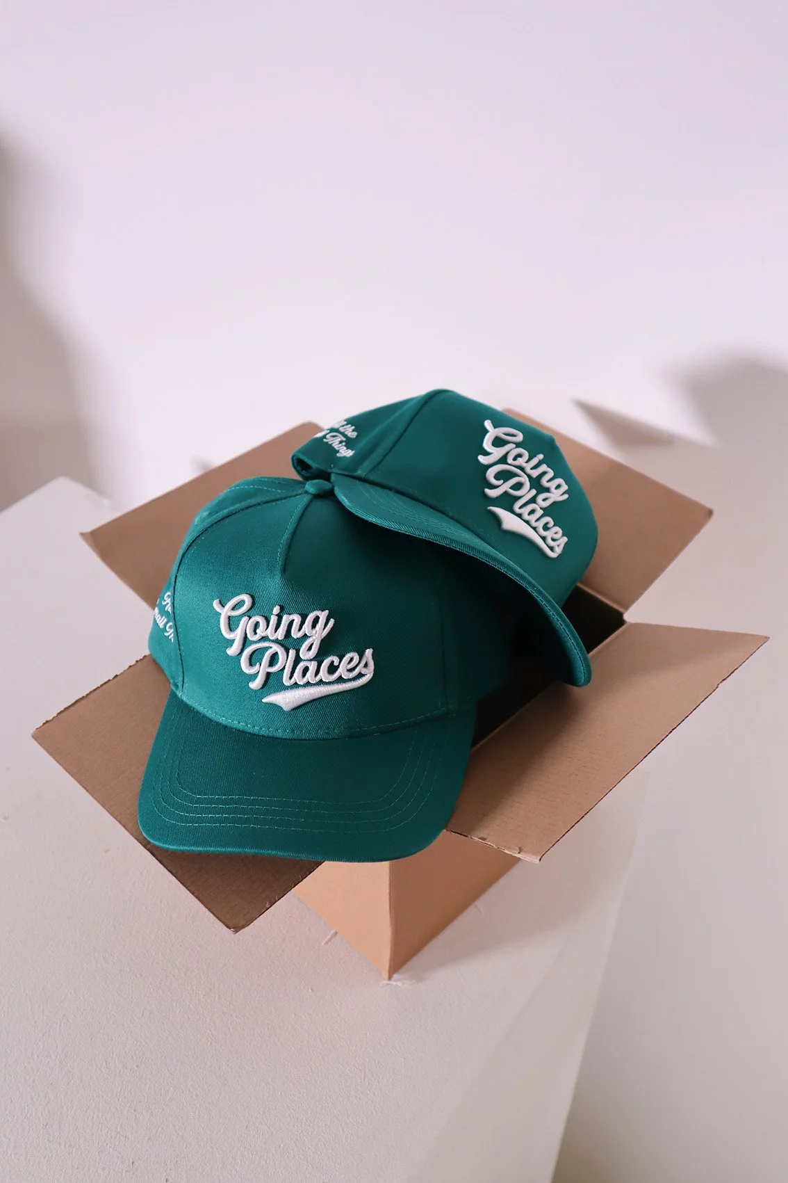 Green baseball caps with words 'Going Places' on top of a cardboard box.