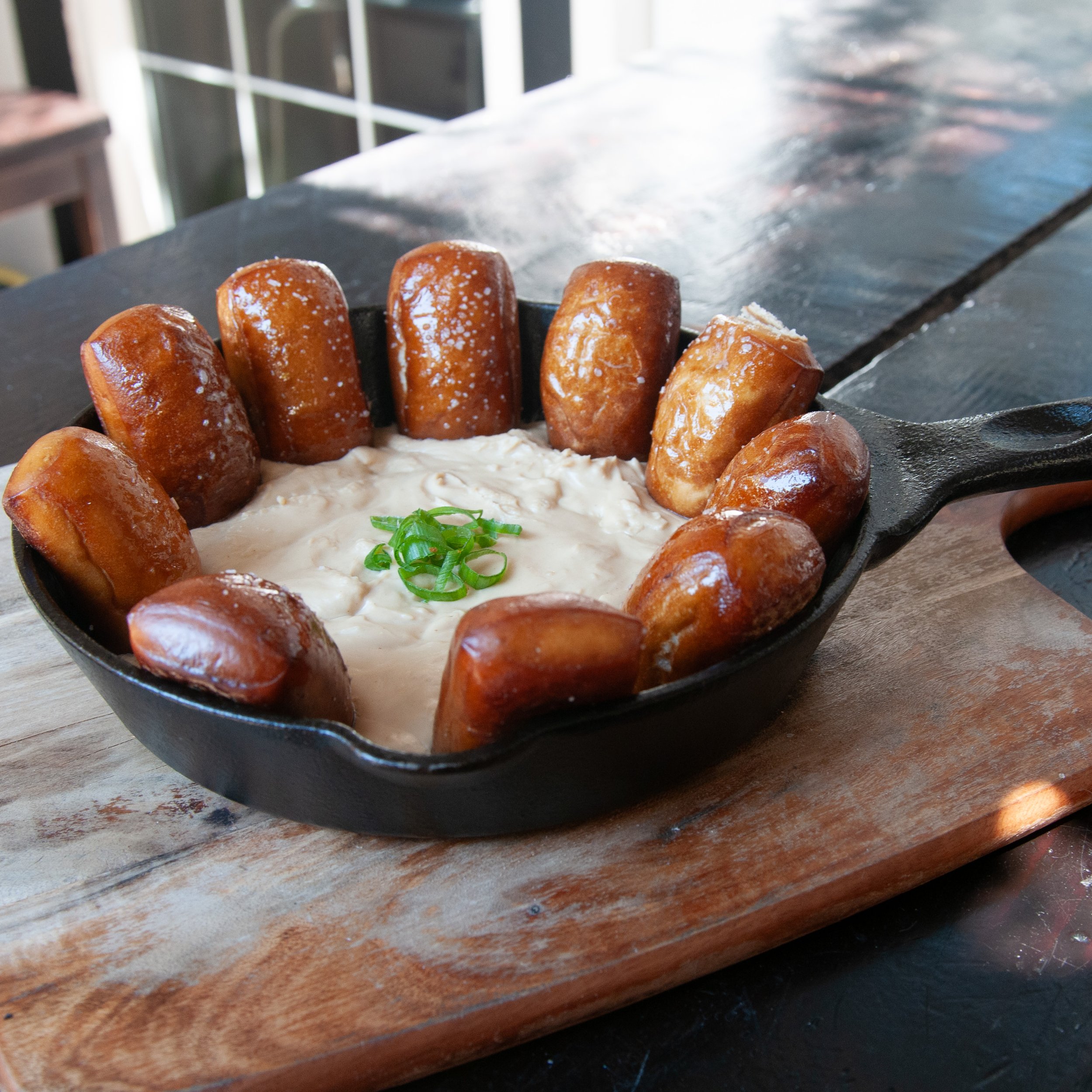 Guinness cheese sauce with pretzel bites in a cast iron skillet served on a wooden board, topped with chopped green onions.