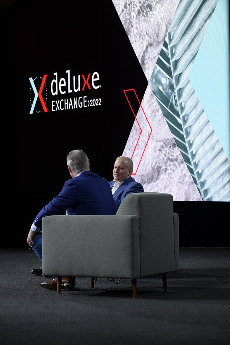 Keynote speakers sitting on stage with digital graphics as a backdrop.