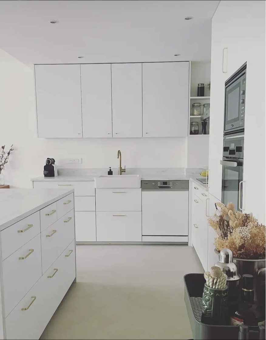 Cuisine contemporaine avec béton ciré au sol, façades blanches, poignées dorées