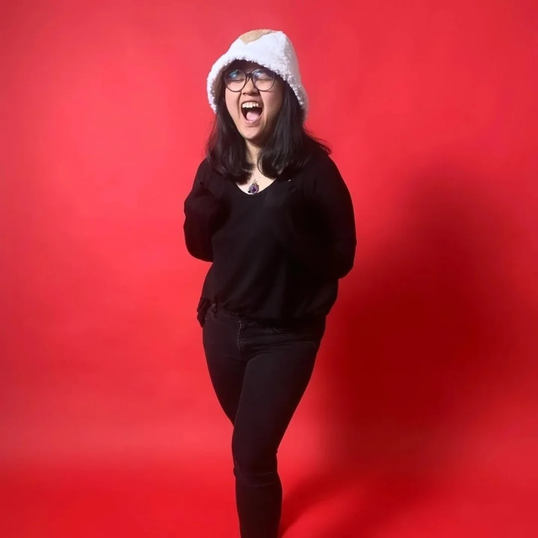 Rosy L smiles while standing in front of a solid red backdrop