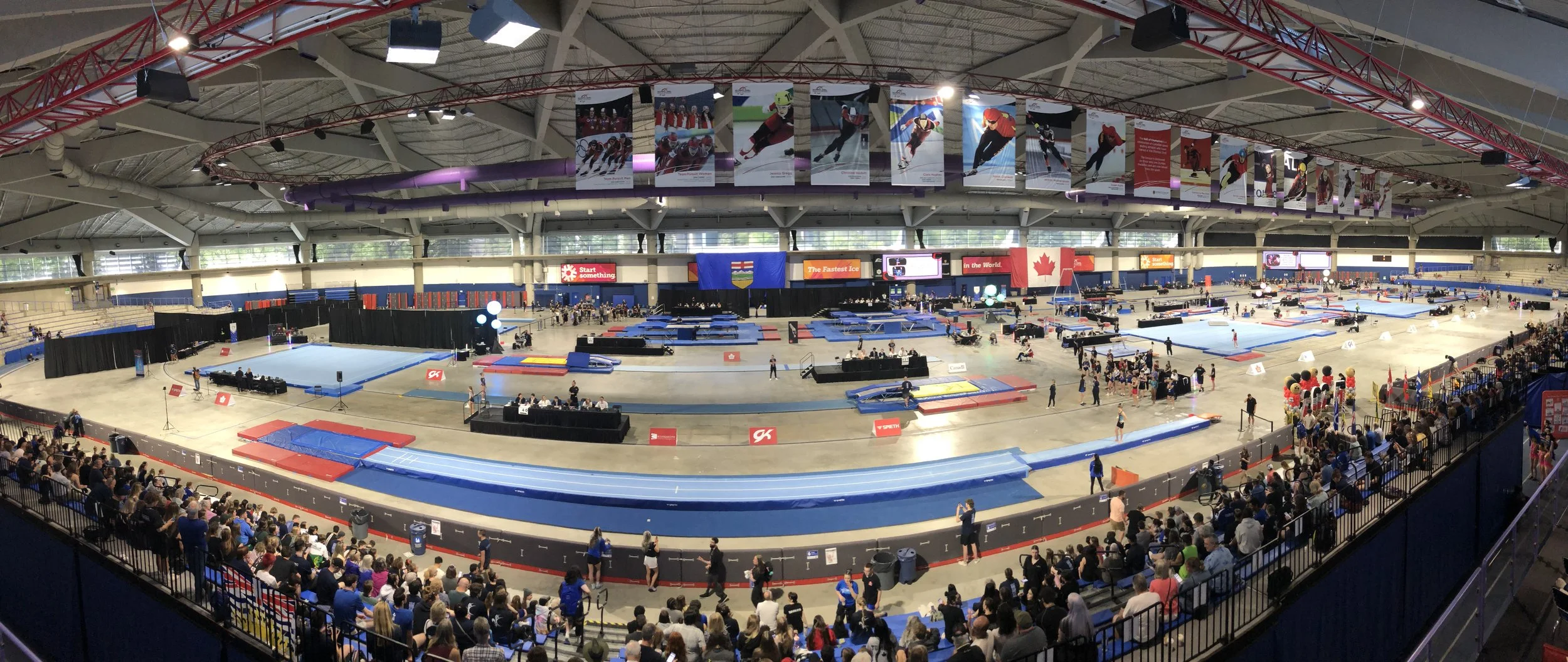 An indoor skating arena filled with spectators, ice skating rinks, and various equipment, with banners of hockey players hanging from the ceiling.