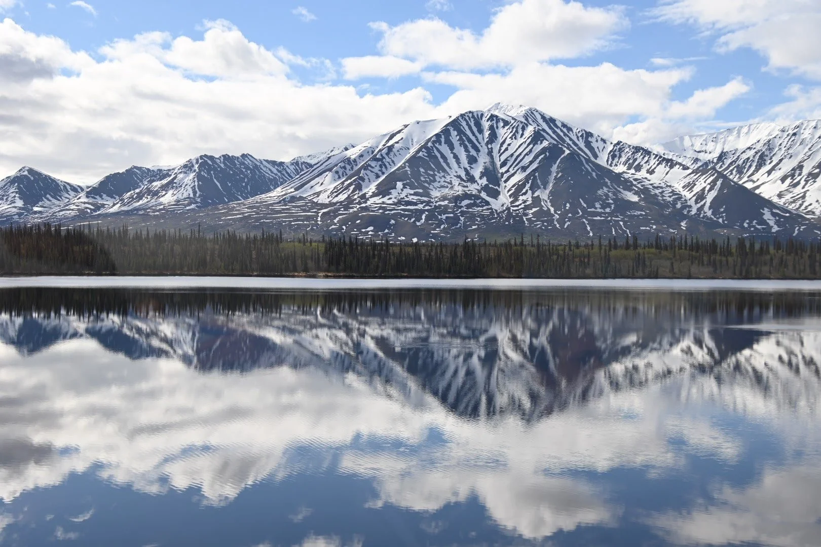 Snow-capped mountains reflected in a calm lake with a partly cloudy sky.