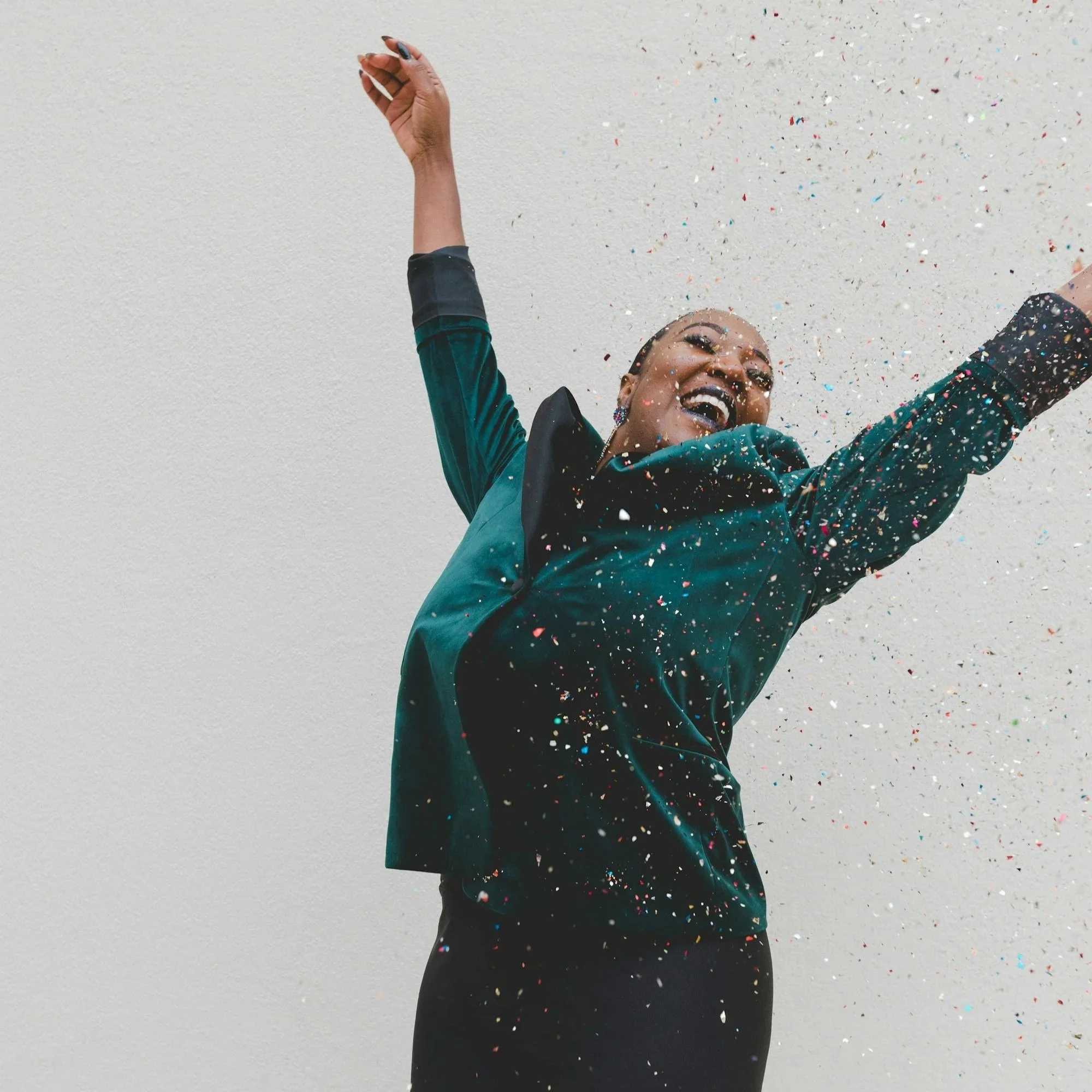 Woman smiling and throwing her hands up in the midst of confetti.