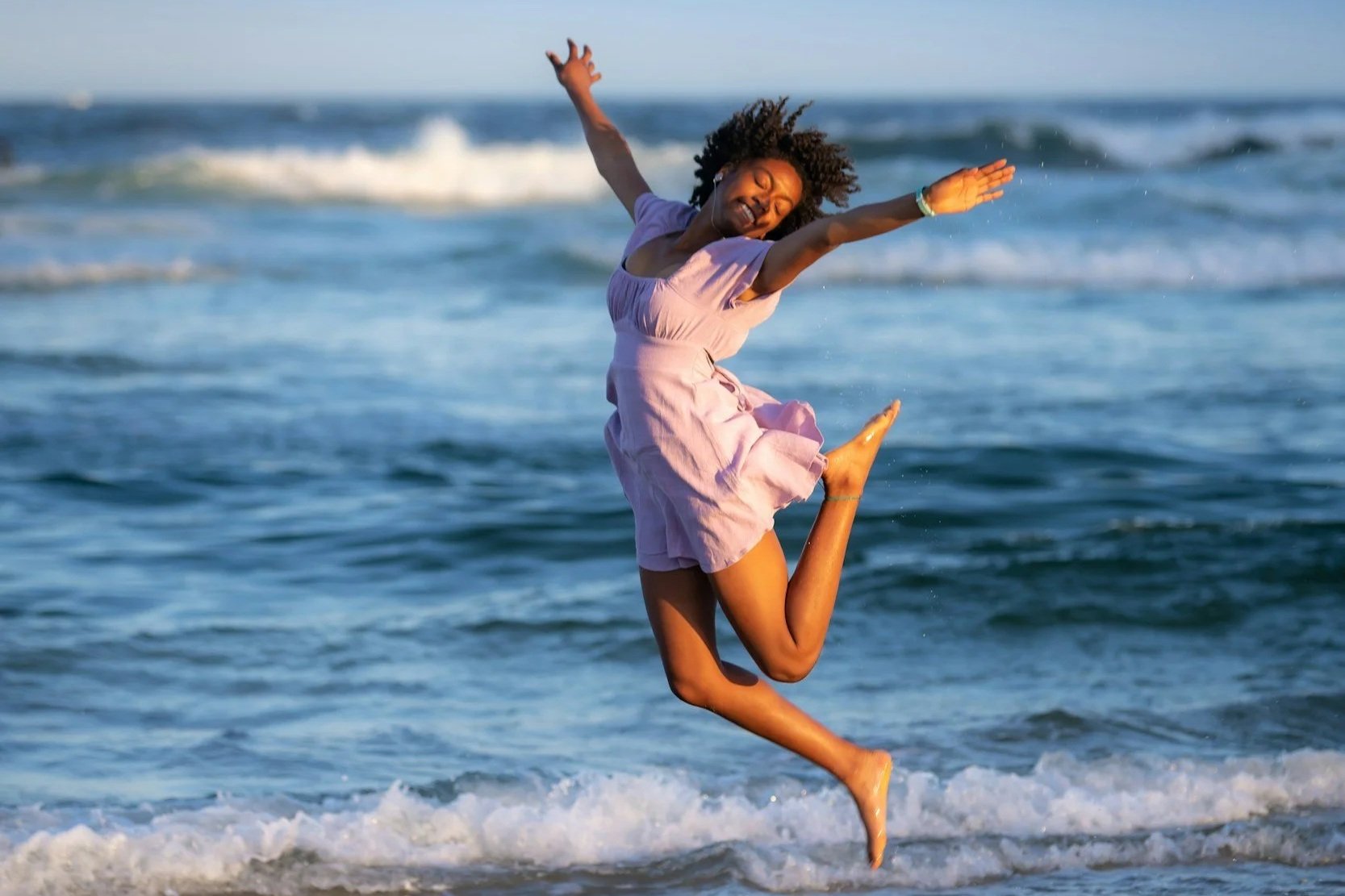 A black mom jumping with excitement on the beach.