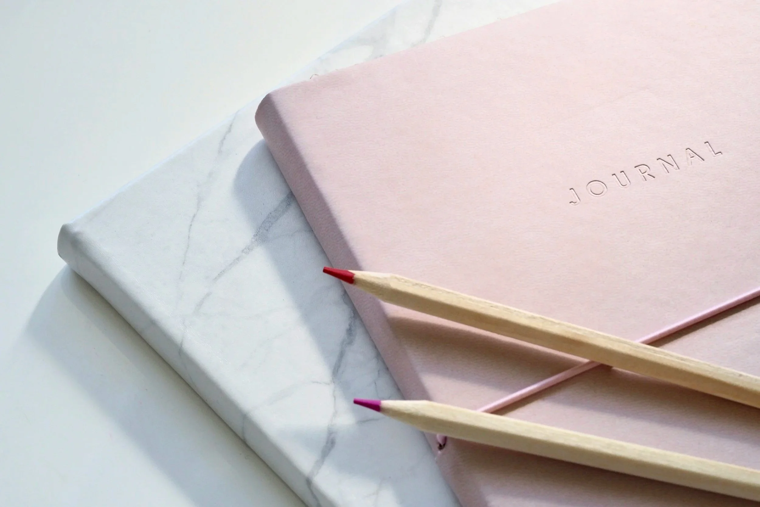 A pink journal sitting on top of a white journal.