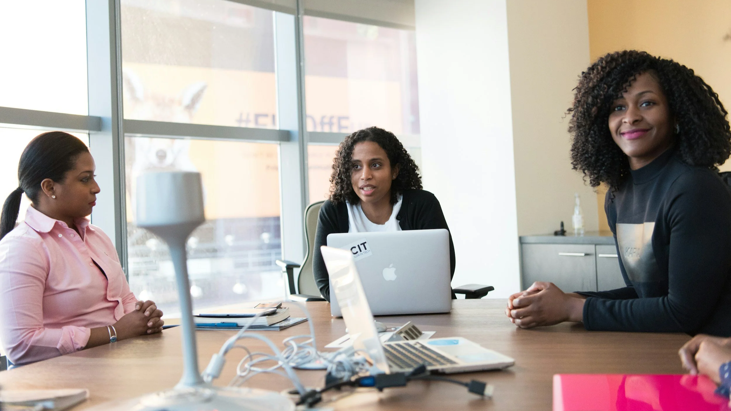 Office scene with African American women sitting at a table with their laptops.
