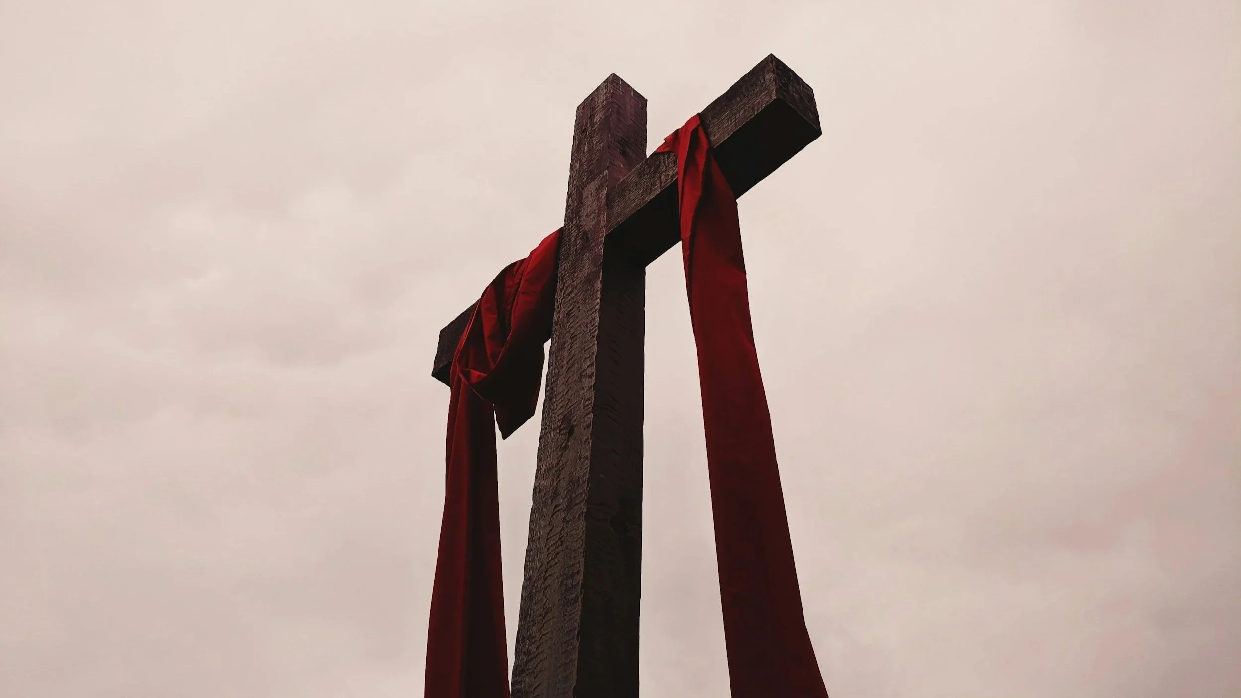 Wooden cross with red sash laying across it.