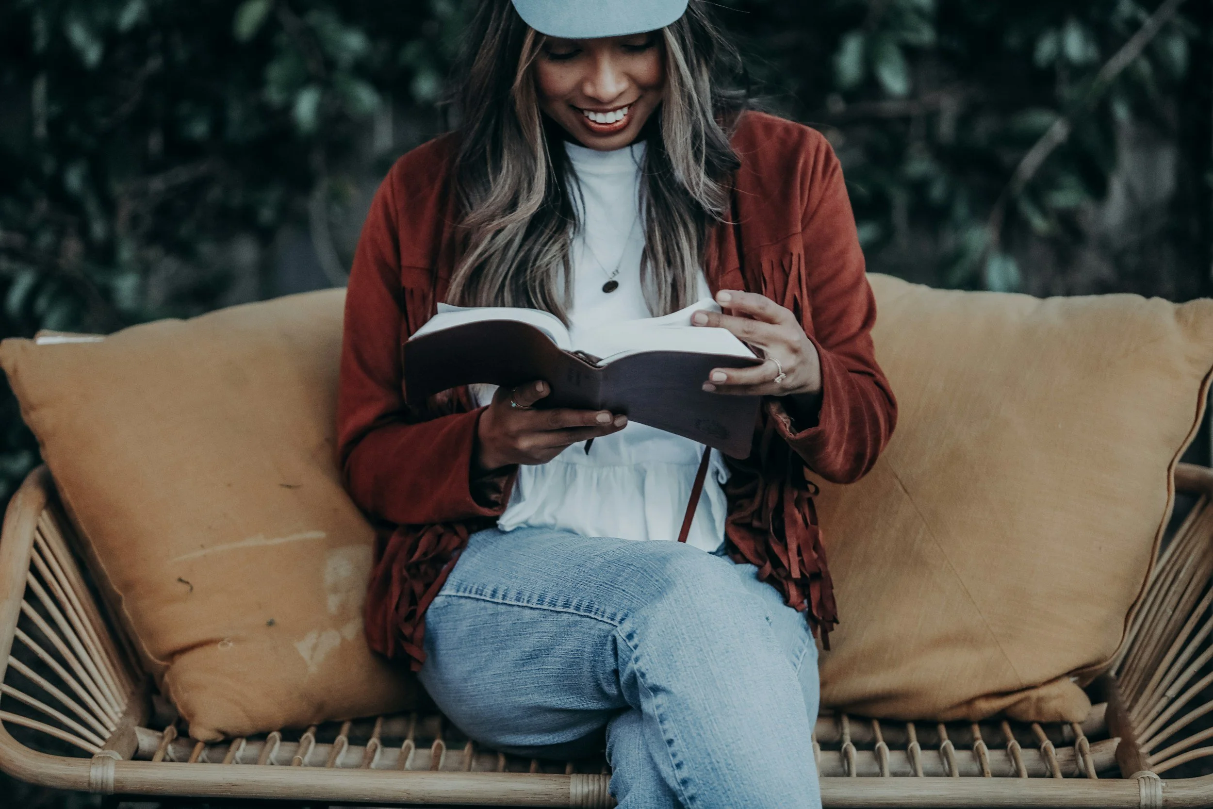 A mother sitting outside dressed in fall clothes smiling and reading her bible.