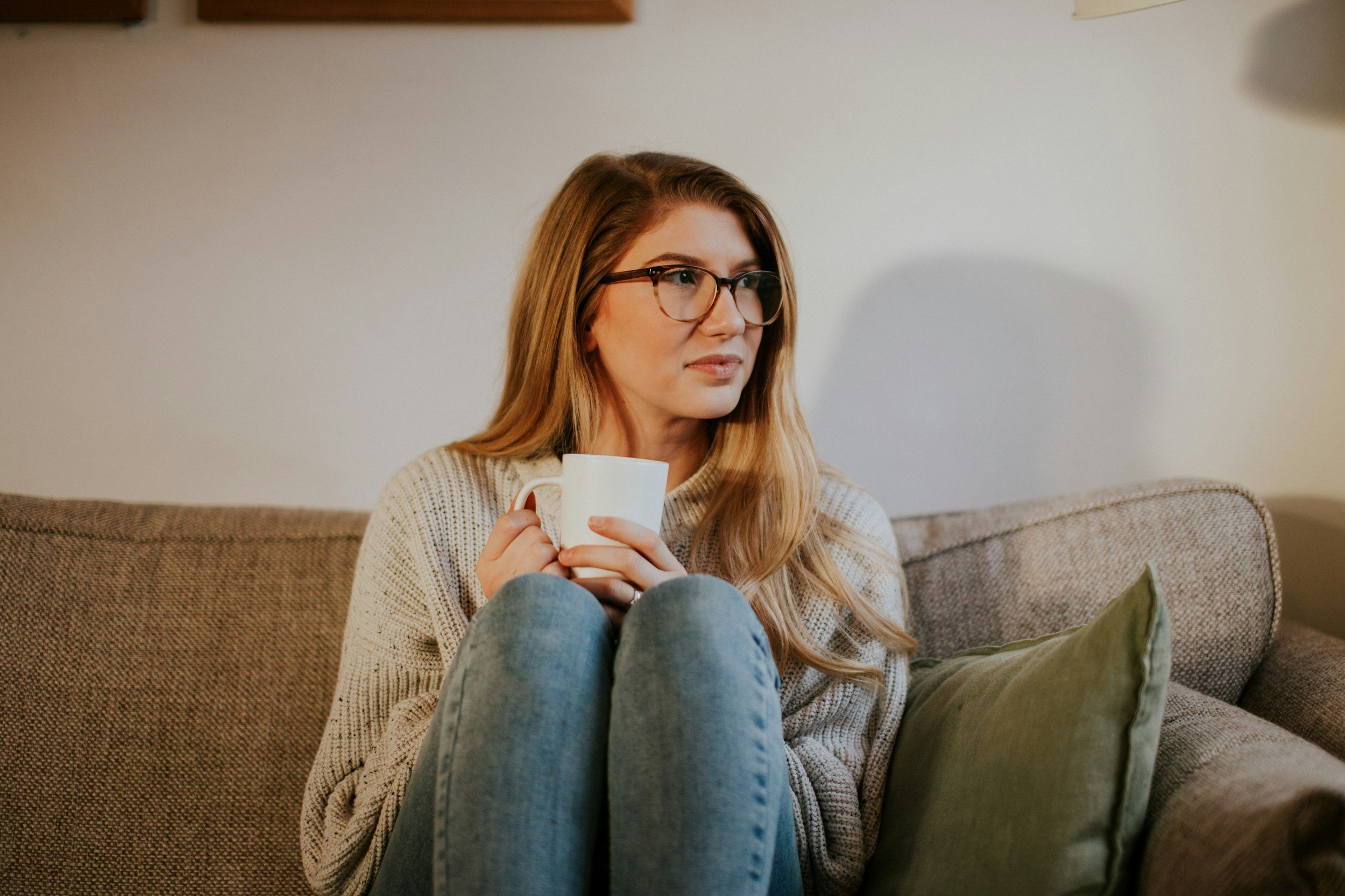 A Caucasian woman sitting alone thinking on the couch with a cup of coffee