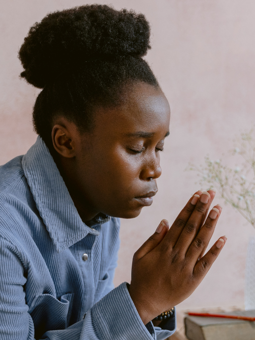 African American mom in blue jacket praying with eyes closed and hands together.