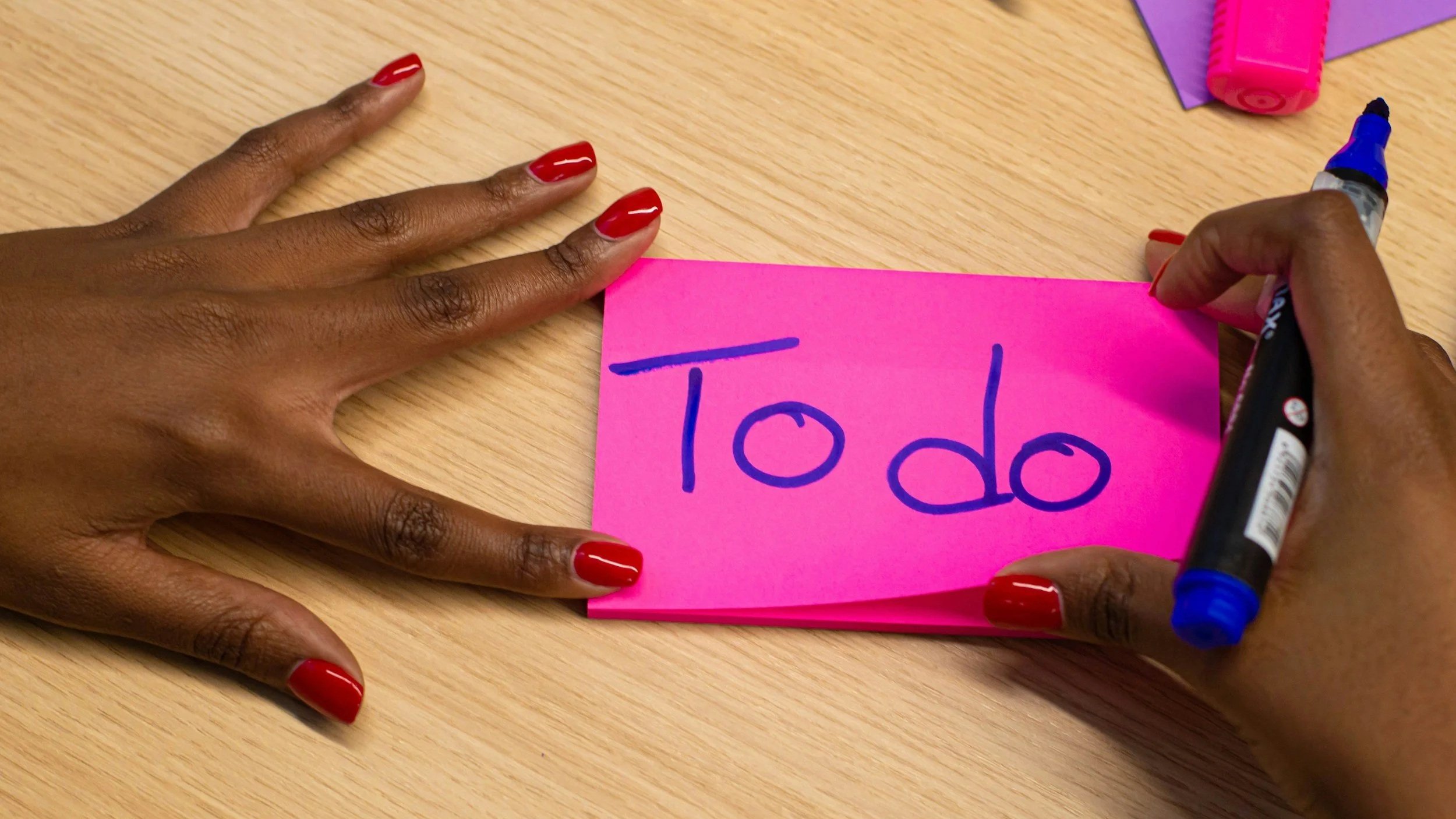 A mother's hands writing the words to do on a pink sticky note.