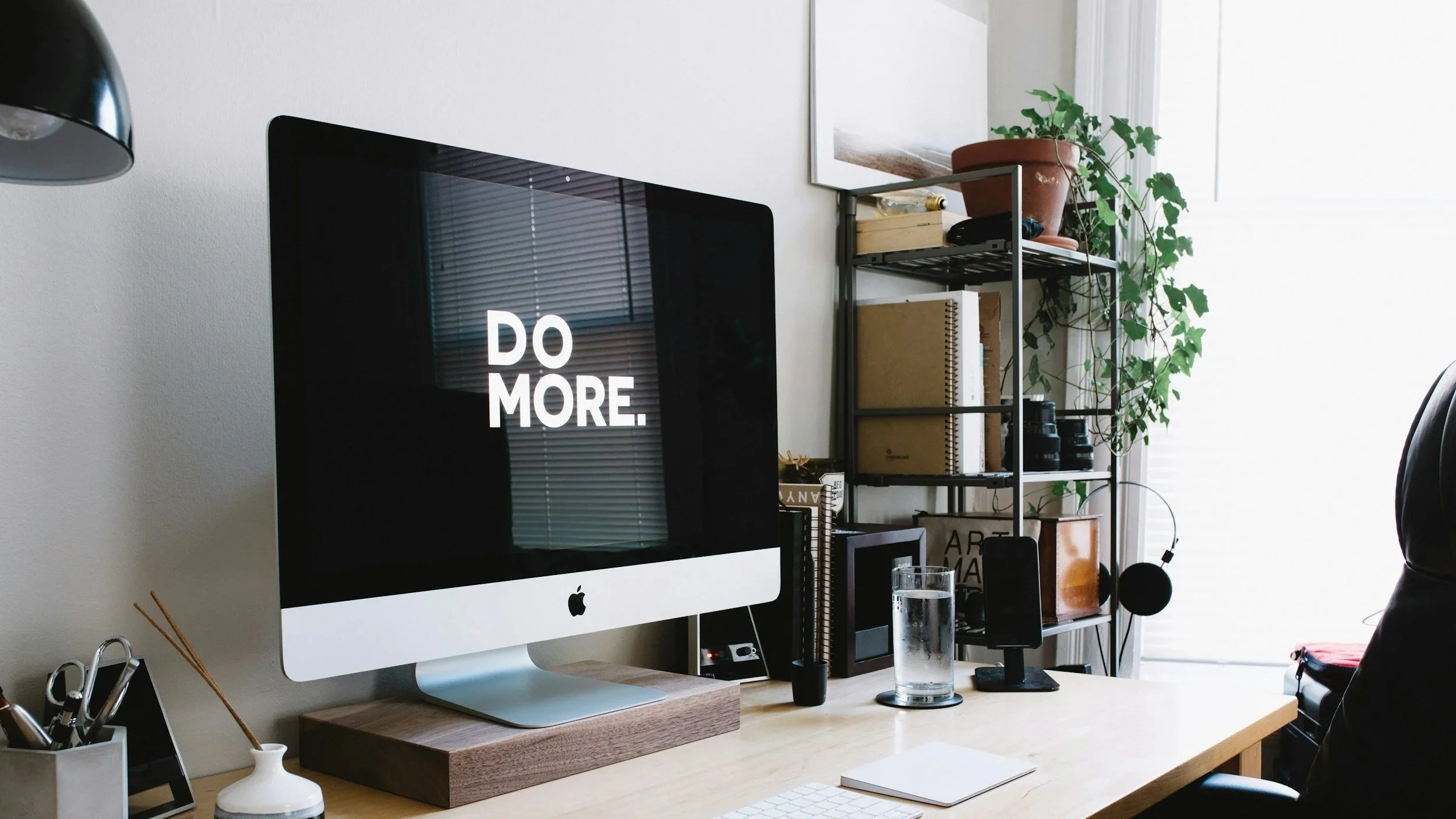 An office desk with an Apple computer with DO MORE typed on the screen.