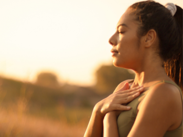 Woman outside in workout clothes, with her hands on her heart taking a deep breath.