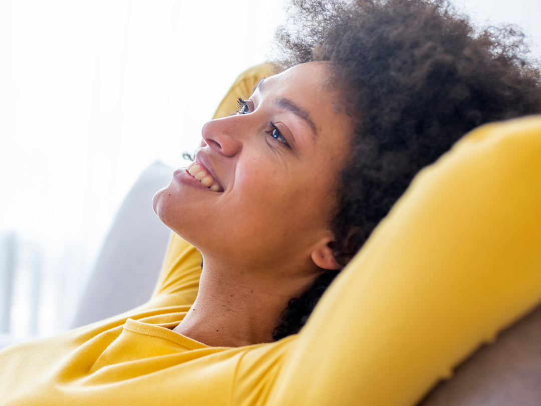 African Amercian woman leaning back on the couch smiling and with her arms behind her head.