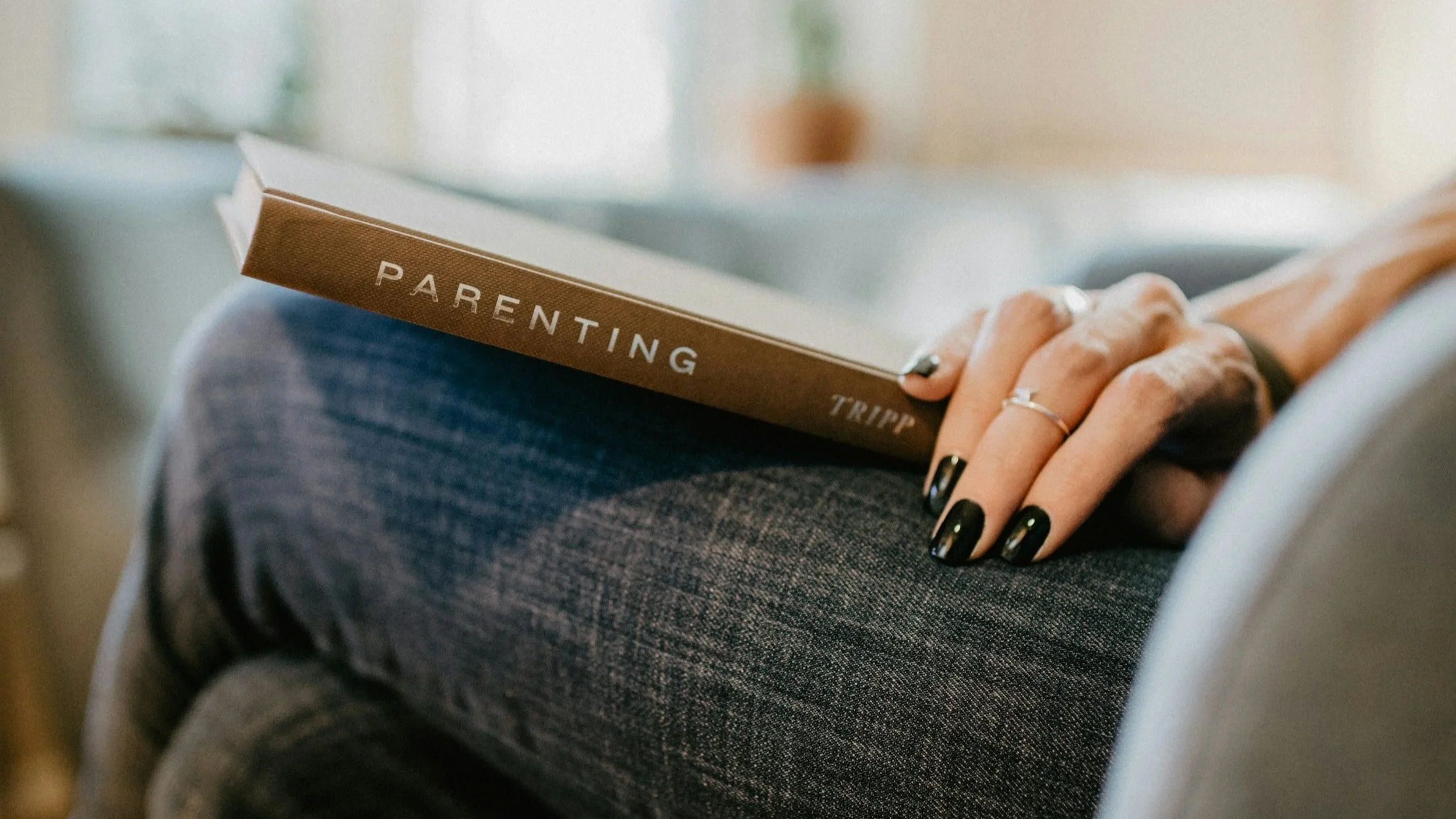 Brown book with the word Parenting on the spine laying in a mother's lap