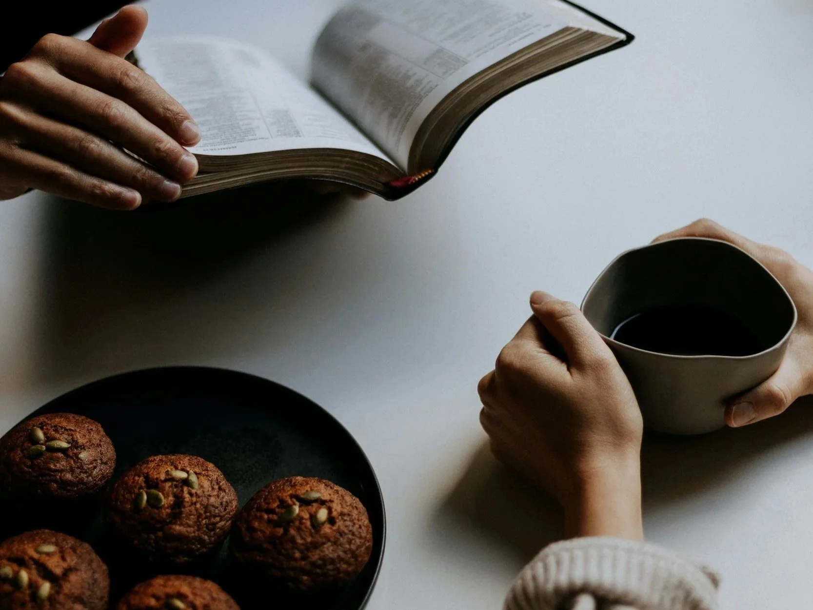 Close up of two women at a table, one holding a cup of coffee and one holding a bible.