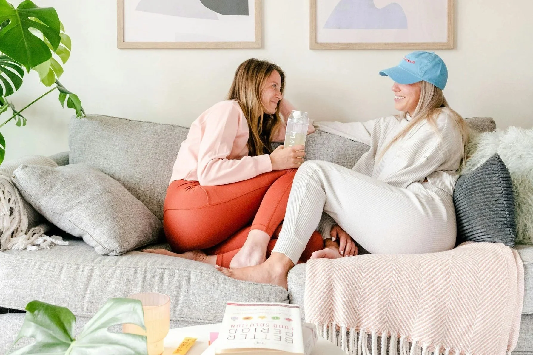 Two moms wearing loungewear sitting on couch talking.