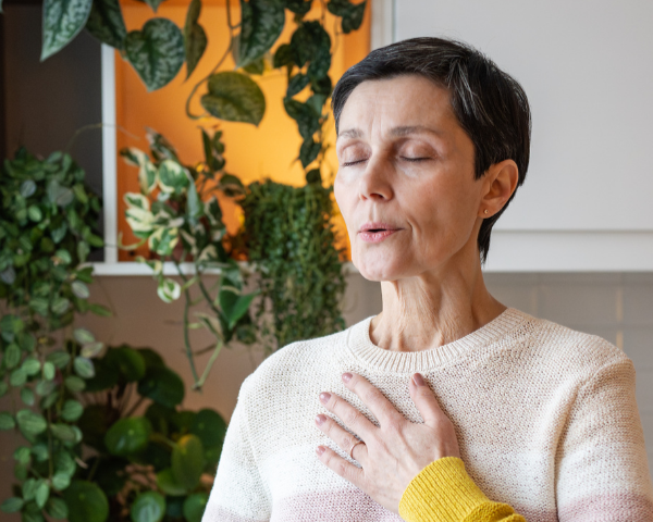 Older Caucasian mom with hand on her chest taking a deep breath.
