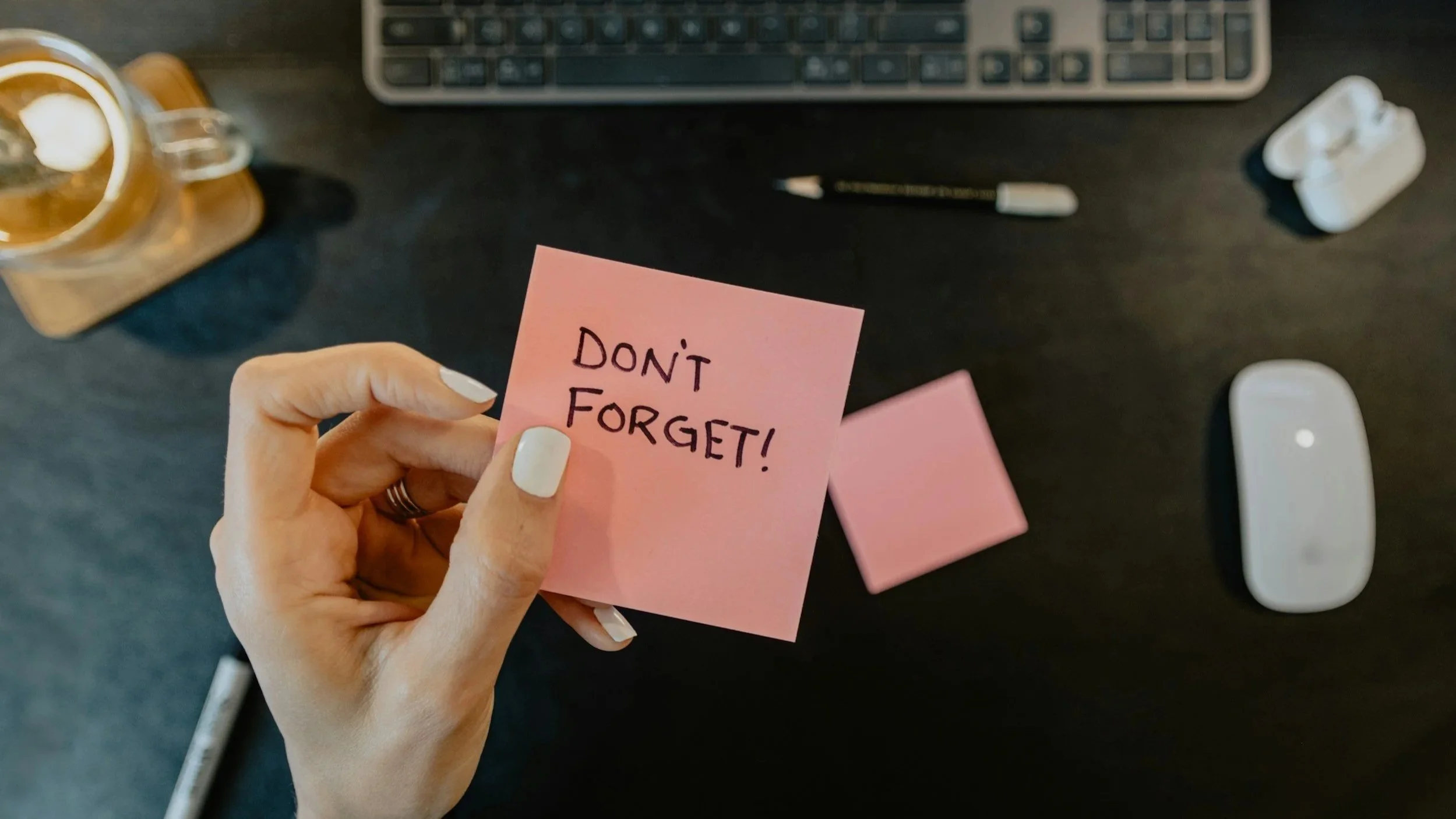 A woman's hand holding a sticky note that says don't forget.