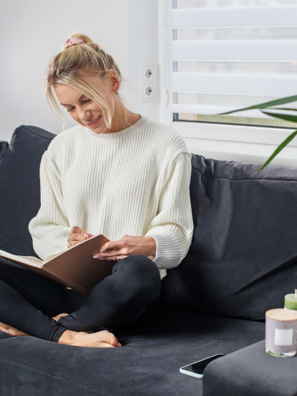 Mom wearing lounge-wear, sitting on couch journaling.