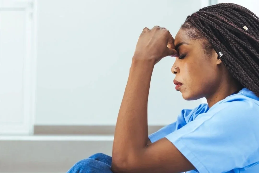 African American doctor sitting on floor with her hands to her head.