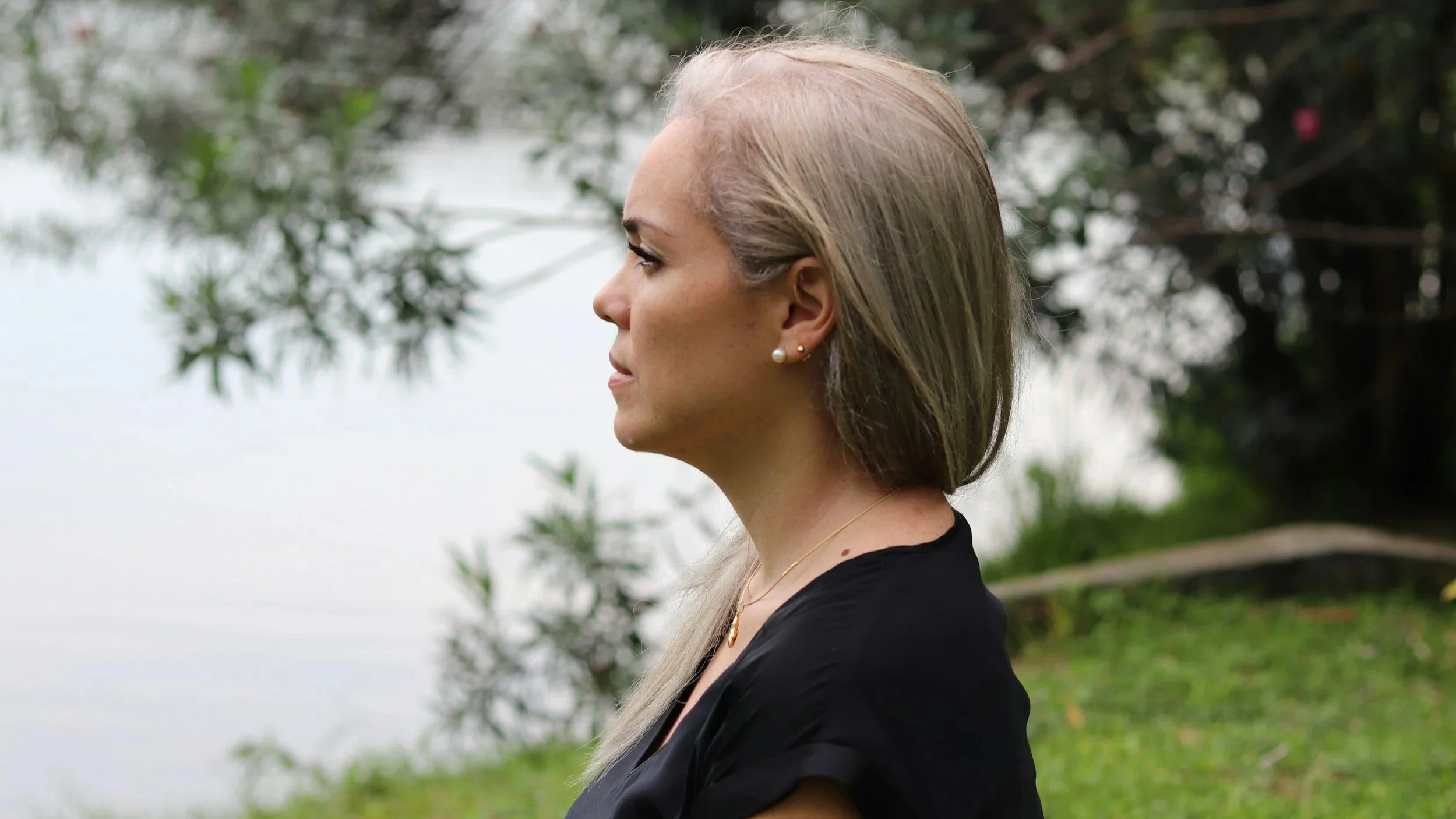 Side profile of Mid-aged Caucasian woman near a lake looking out at the distance.