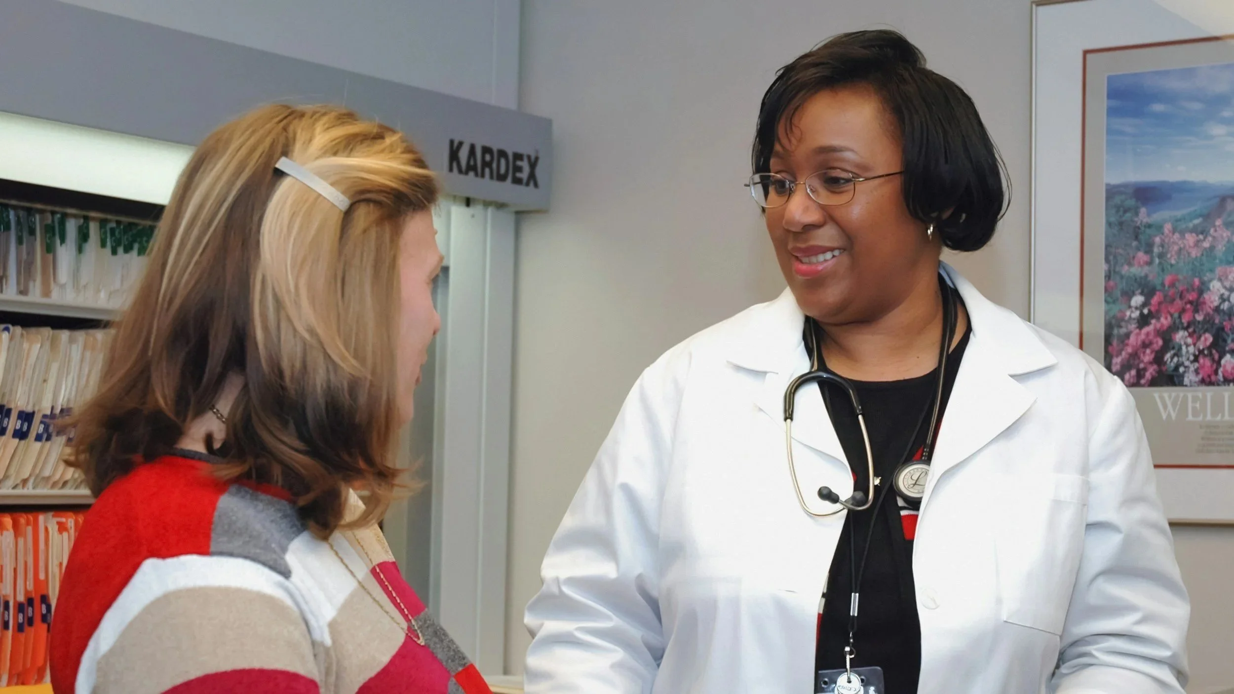 Caucasian woman sitting in a doctor's office with an African American female doctor.