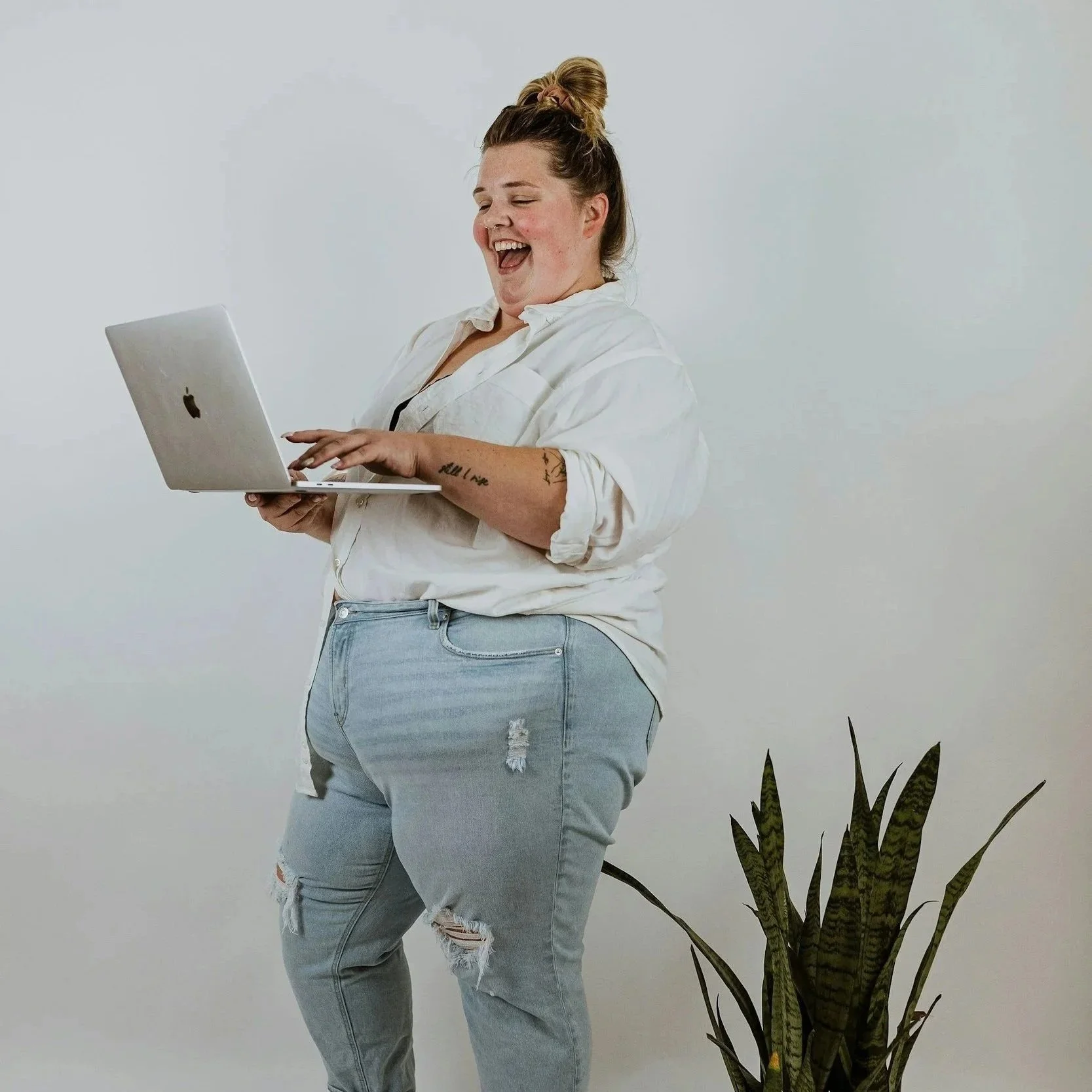 Caucasian, plus size mom with ripped jeans, smiling holding a laptop.