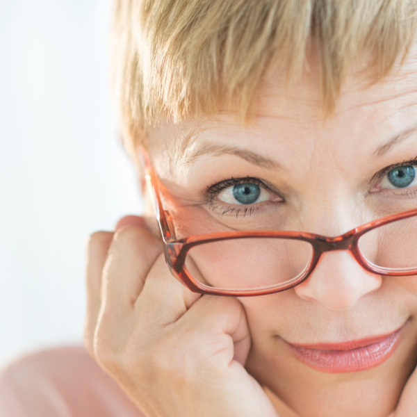 Caucasian woman with short hair glasses and hands on the side of her face.