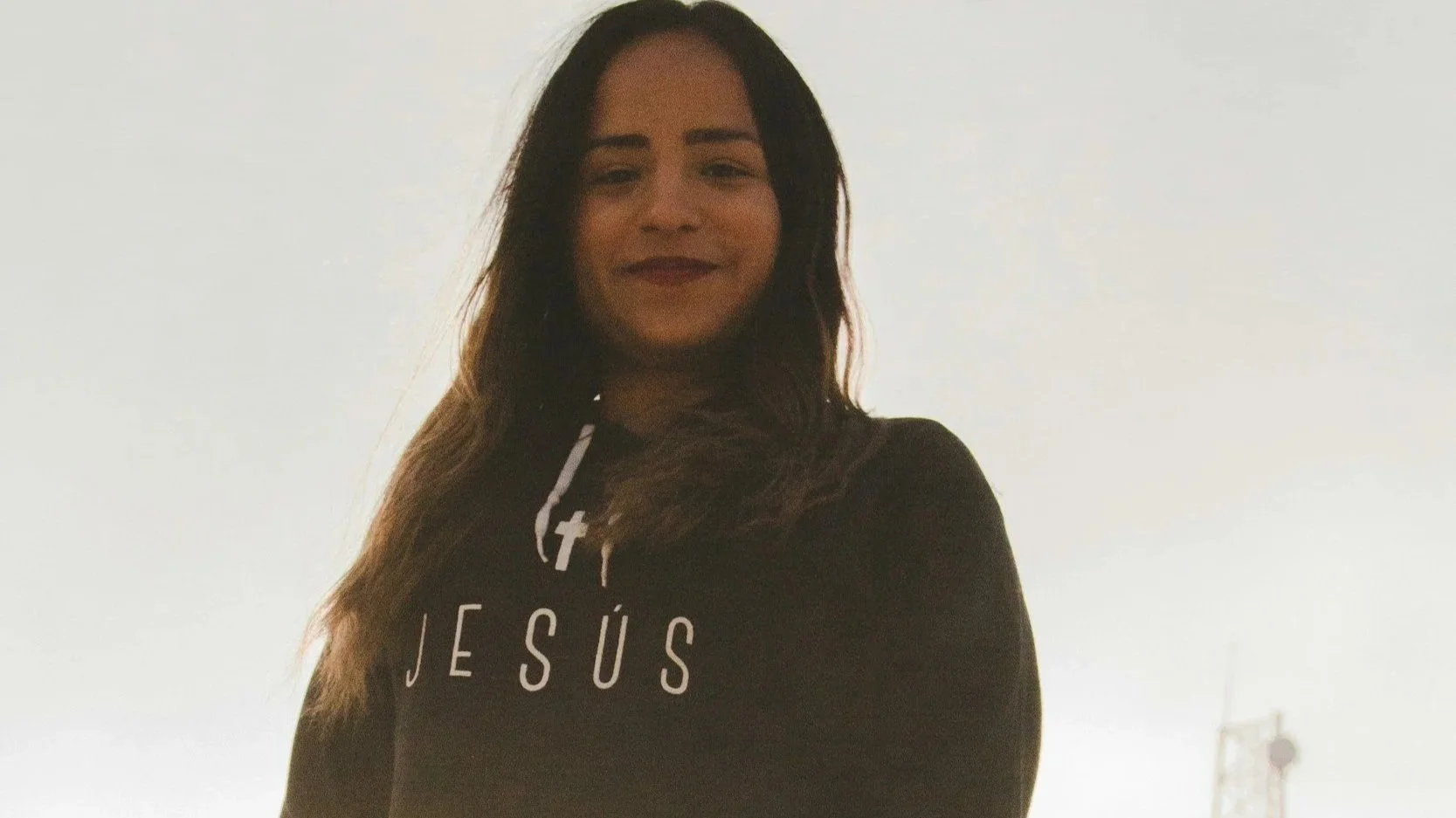Hispanic woman standing outside alone with a hoodie that says Jesus.