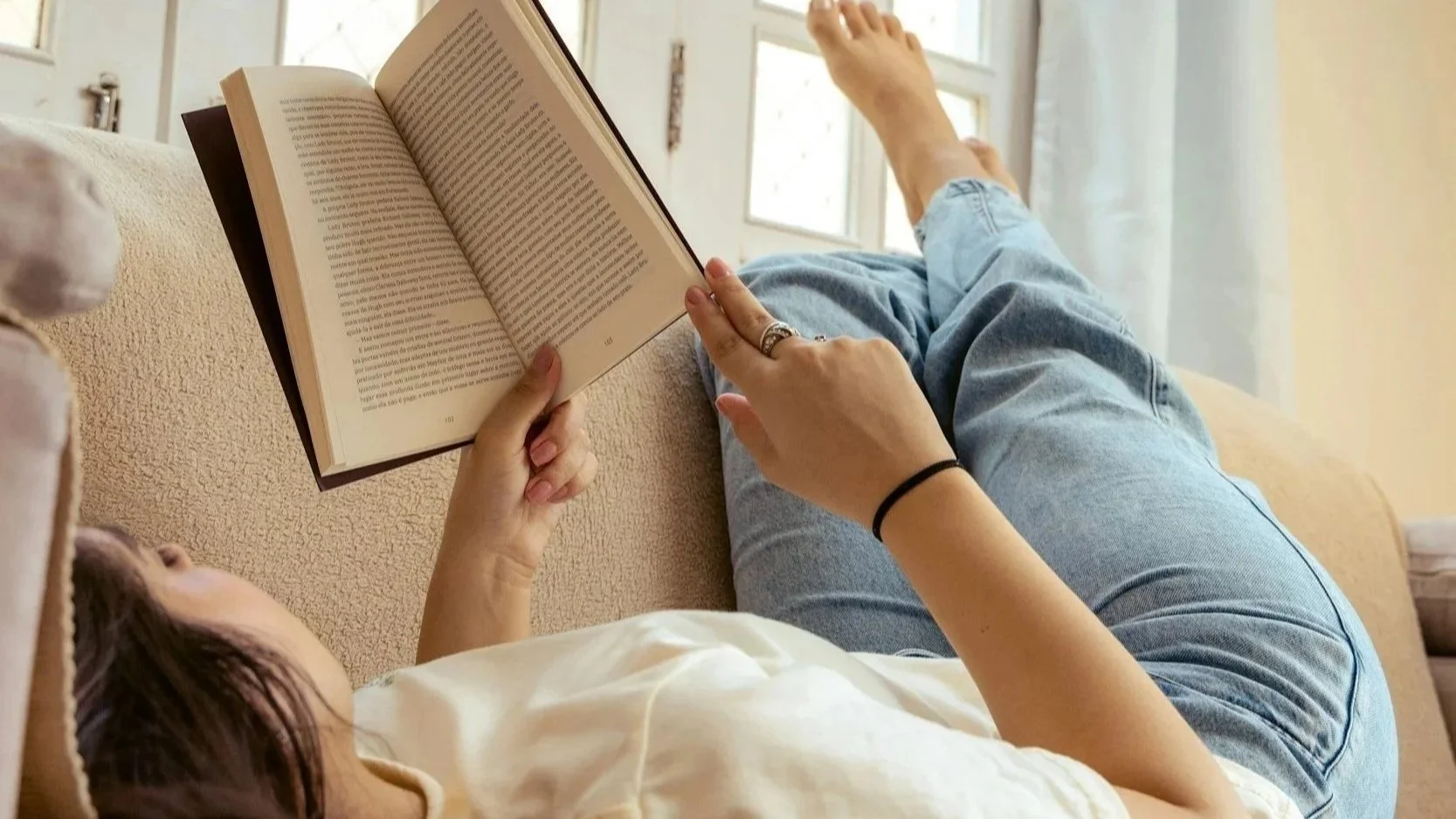 Mother lying on couch reading a book.