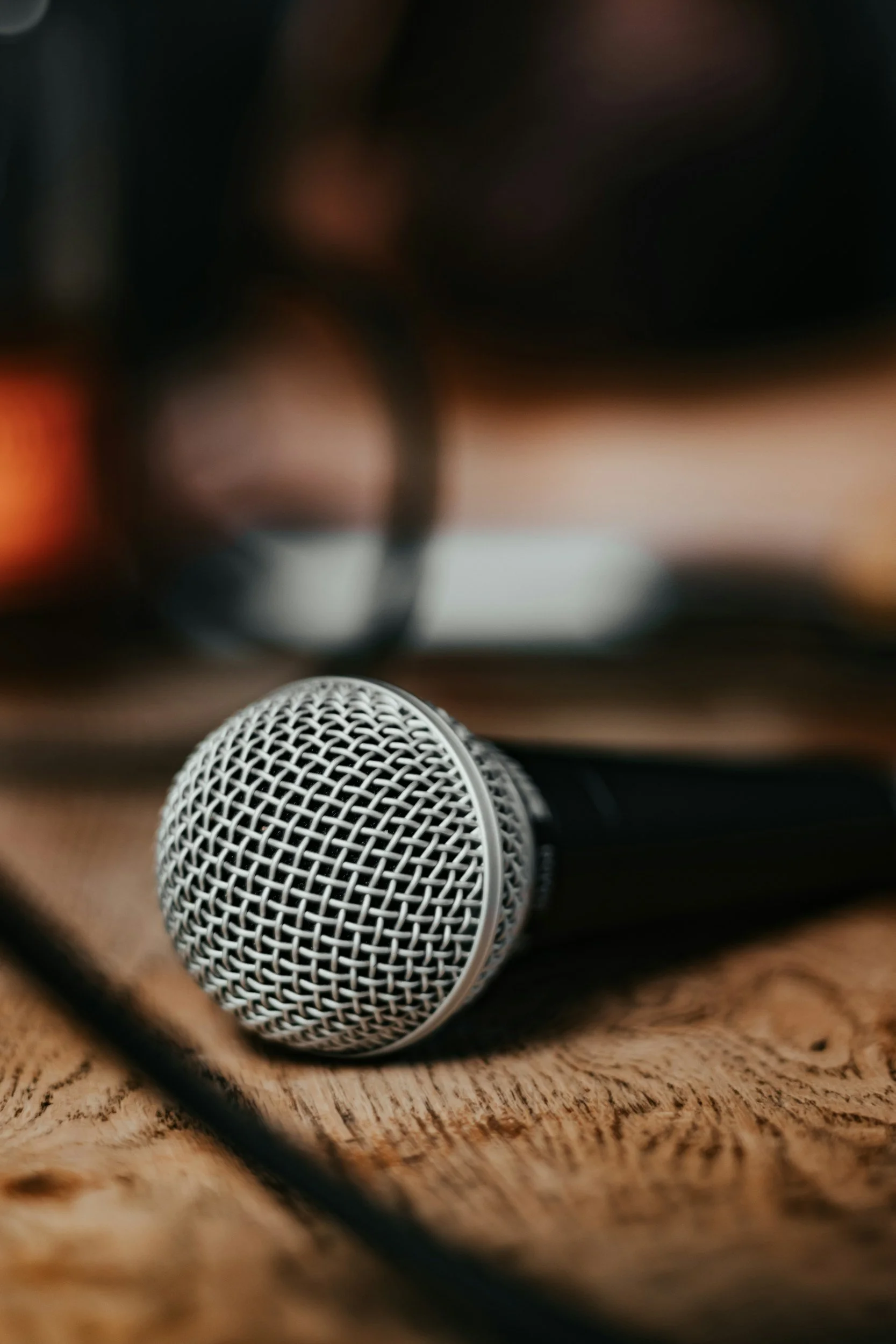 A close-up of a silver microphone on a wooden surface, with a blurred background.