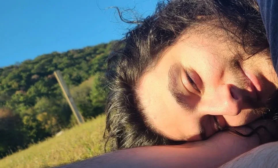 Anthony Ziello lying on a grassy field with a hill and blue sky in the background, relaxing and enjoying the sunlight.
