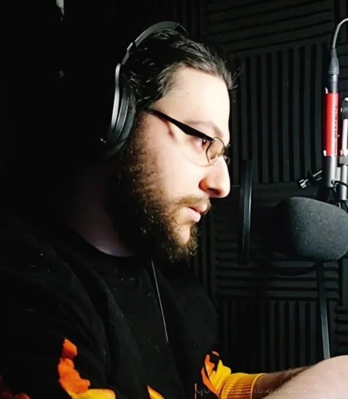 Anthony Ziello with glasses and a beard recording in a sound treated studio with a microphone and headphones.