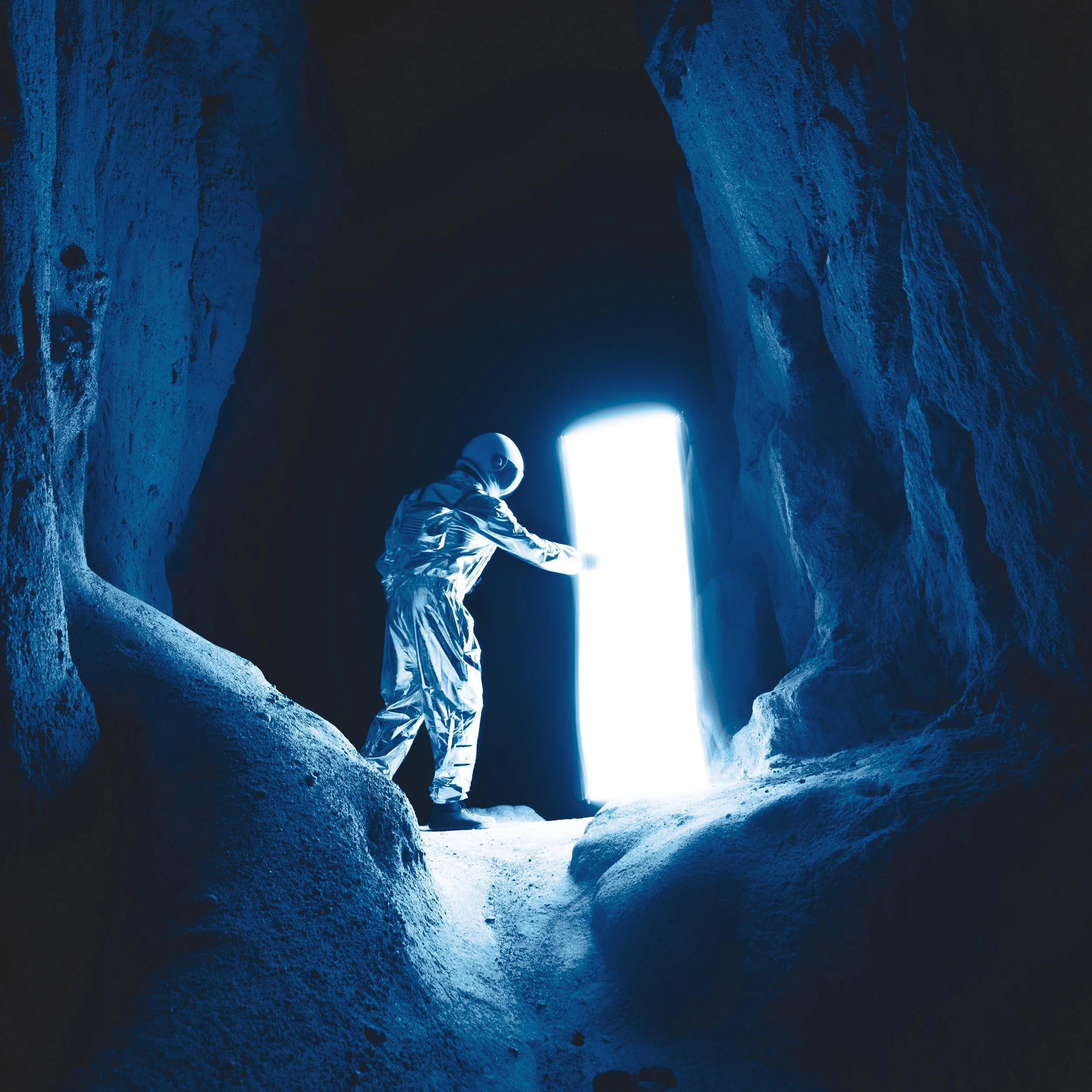 An astronaut in a reflective suit and helmet is inside a rocky cave, opening a glowing doorway that emits bright white light.