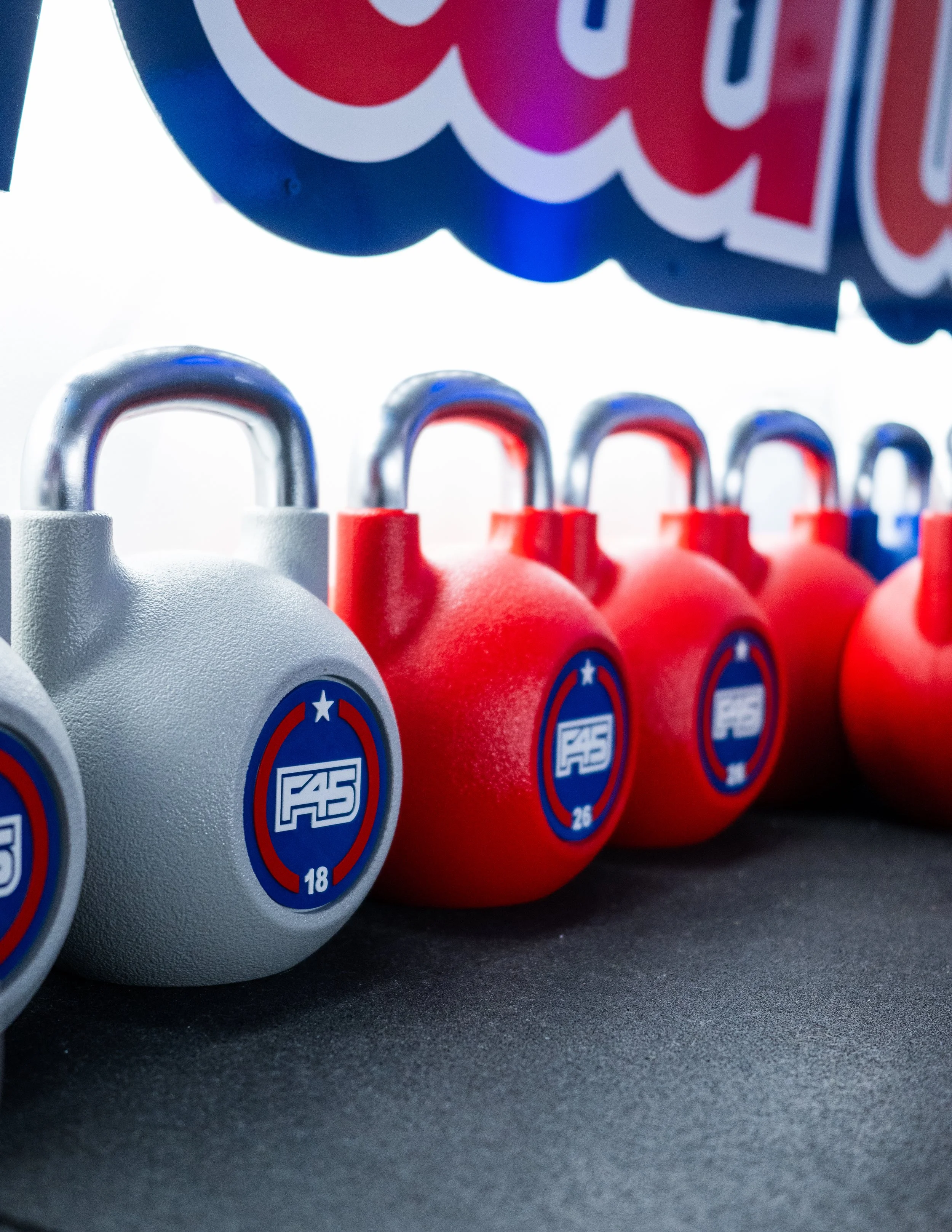 Line of gray and red kettlebells with blue and white logos, with a partly visible colorful sign above them.