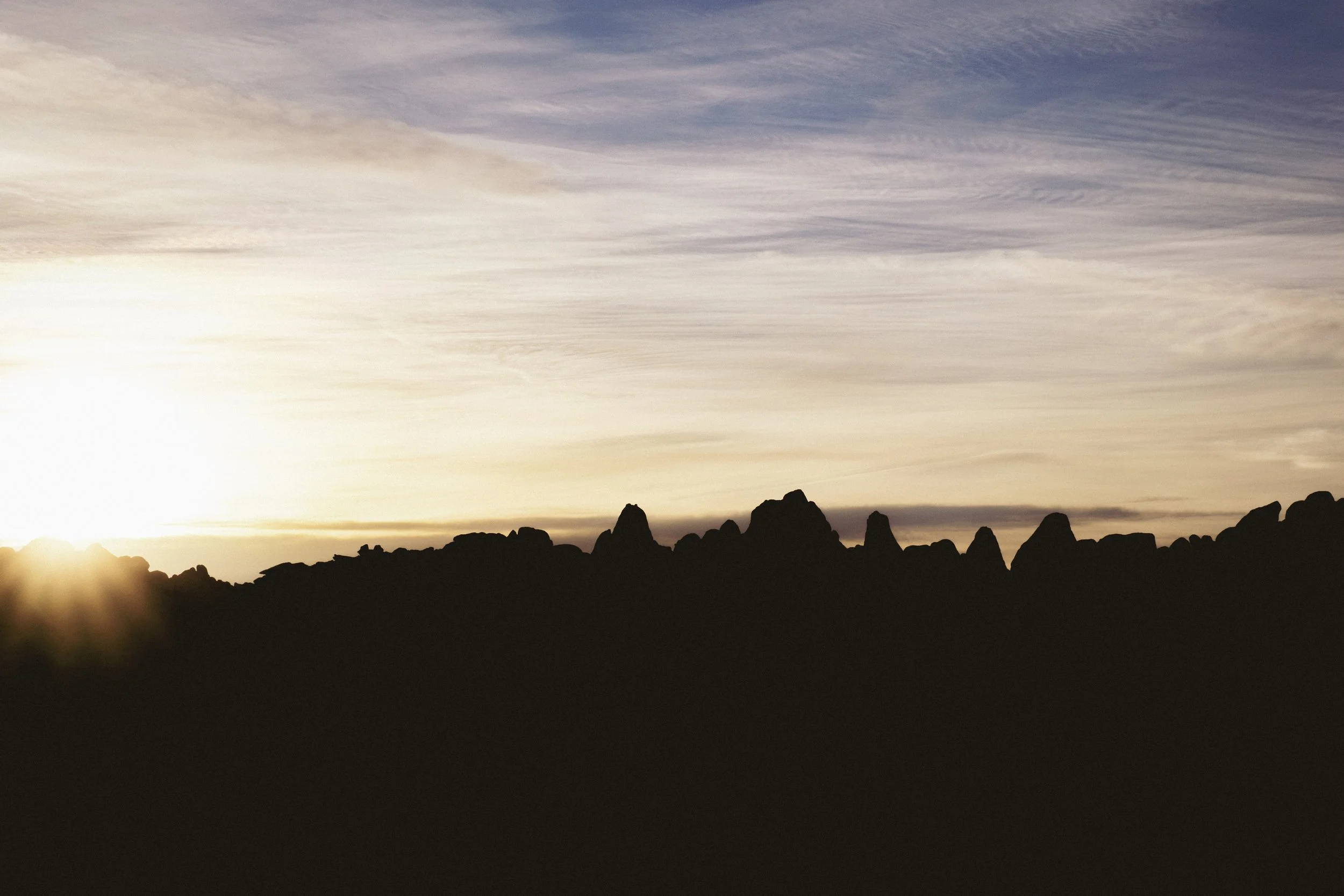 Silhouette of rocky mountains at sunset with a sky filled with wispy clouds.