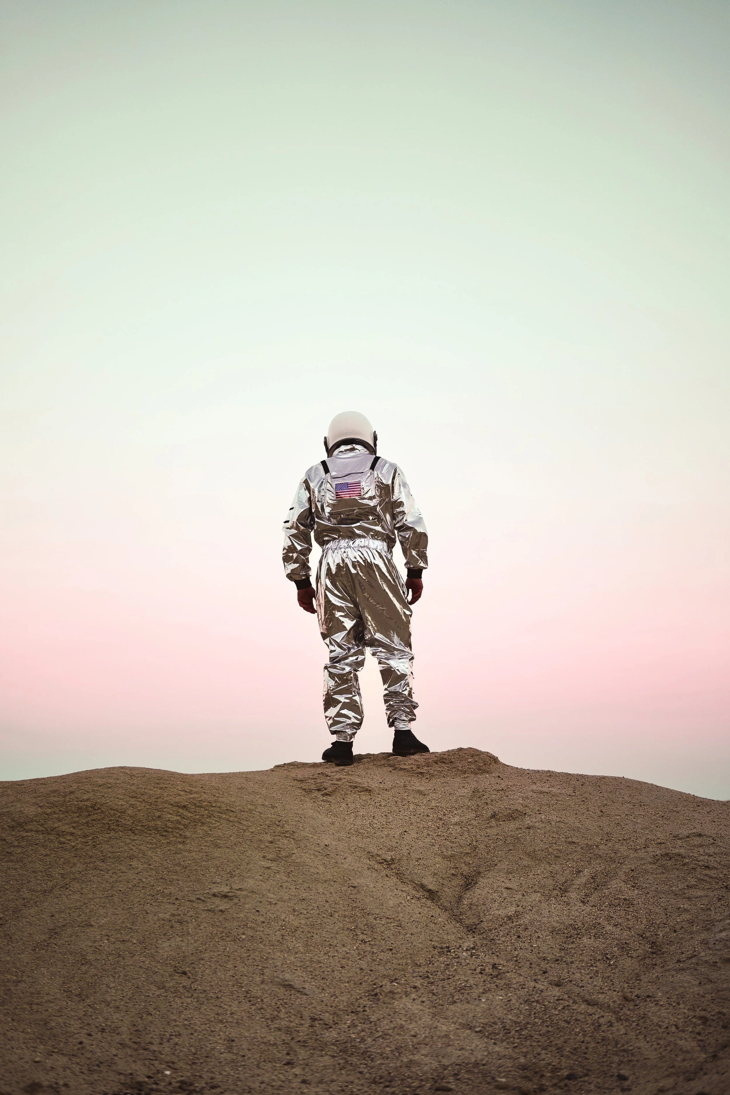 An astronaut standing on a dirt hill with a pastel-colored sky in the background.