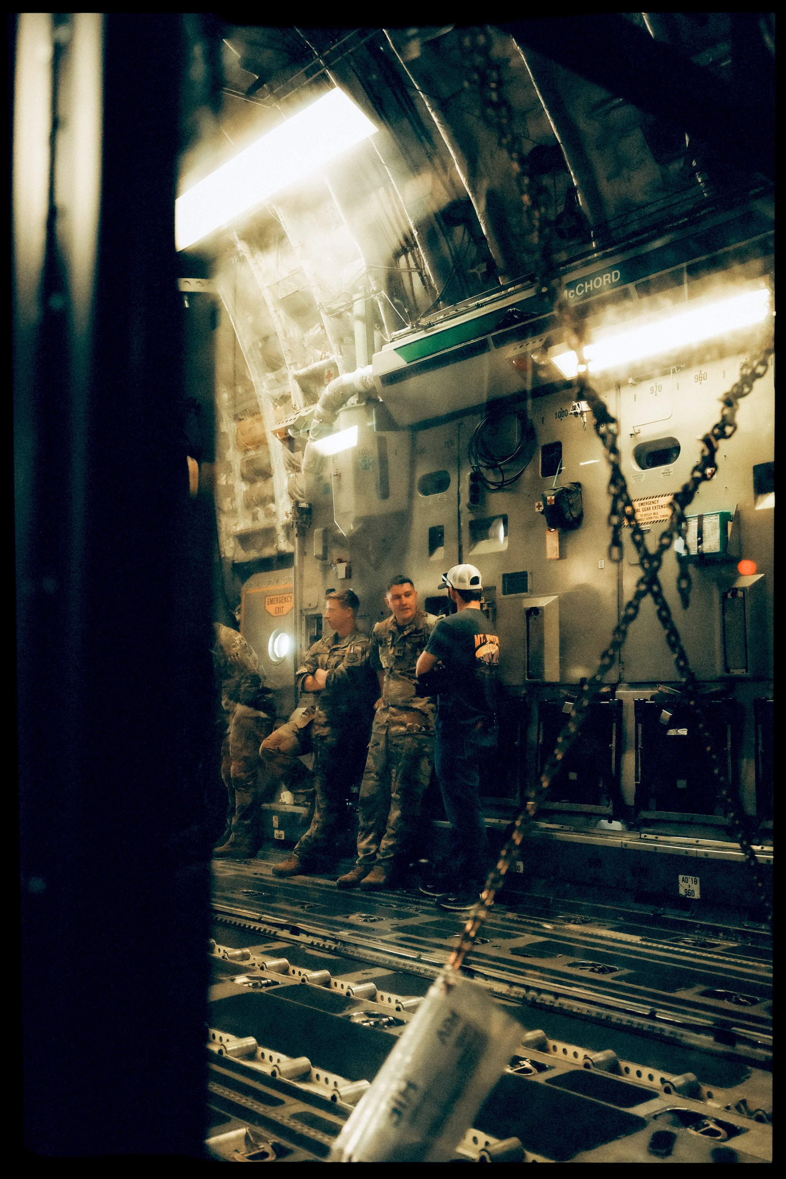 Military personnel in uniform inside an aircraft or spacecraft, seen through a window with chains hanging in the foreground.