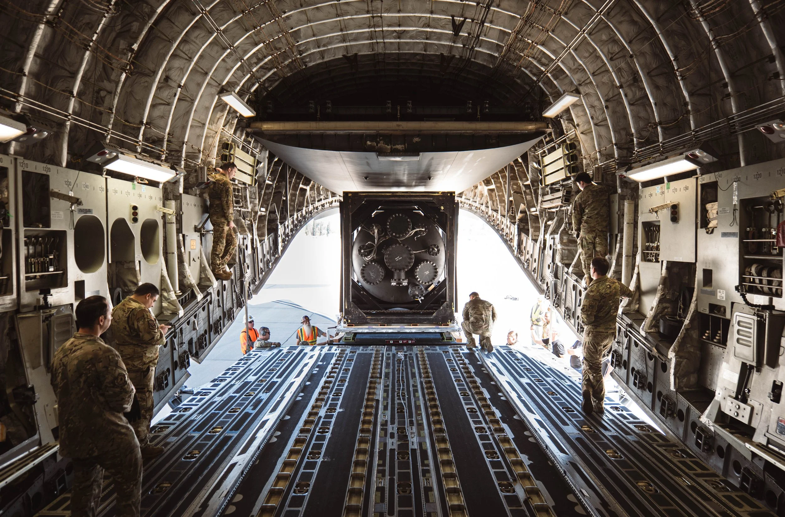 Northern Lights (aurora borealis) over a snow-covered landscape with trees and hills under a starry sky.