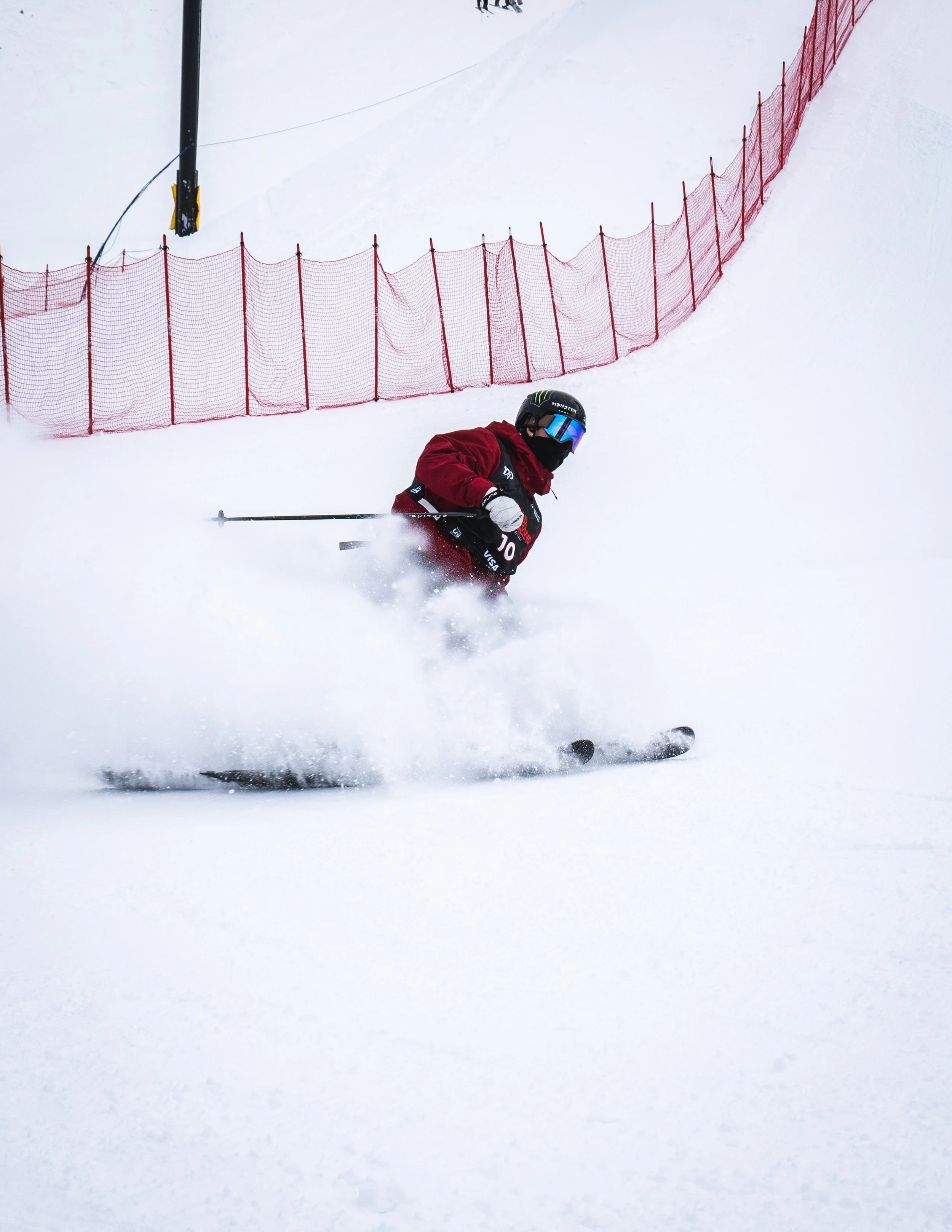 A skier in red gear and a black helmet skiing down a snowy slope near a red safety net.