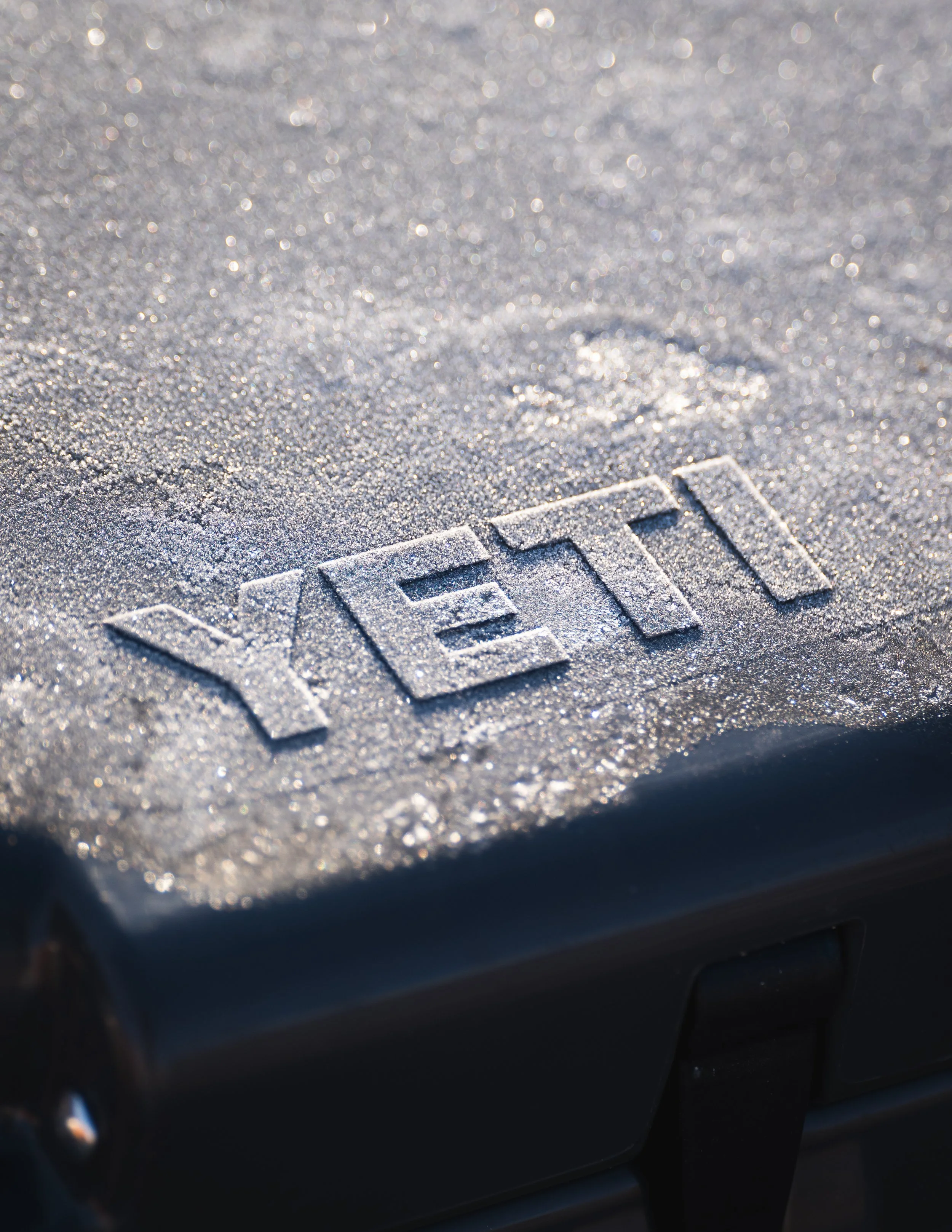 Close-up of a car's surface covered in frost with the word 'VETI' carved into the ice.