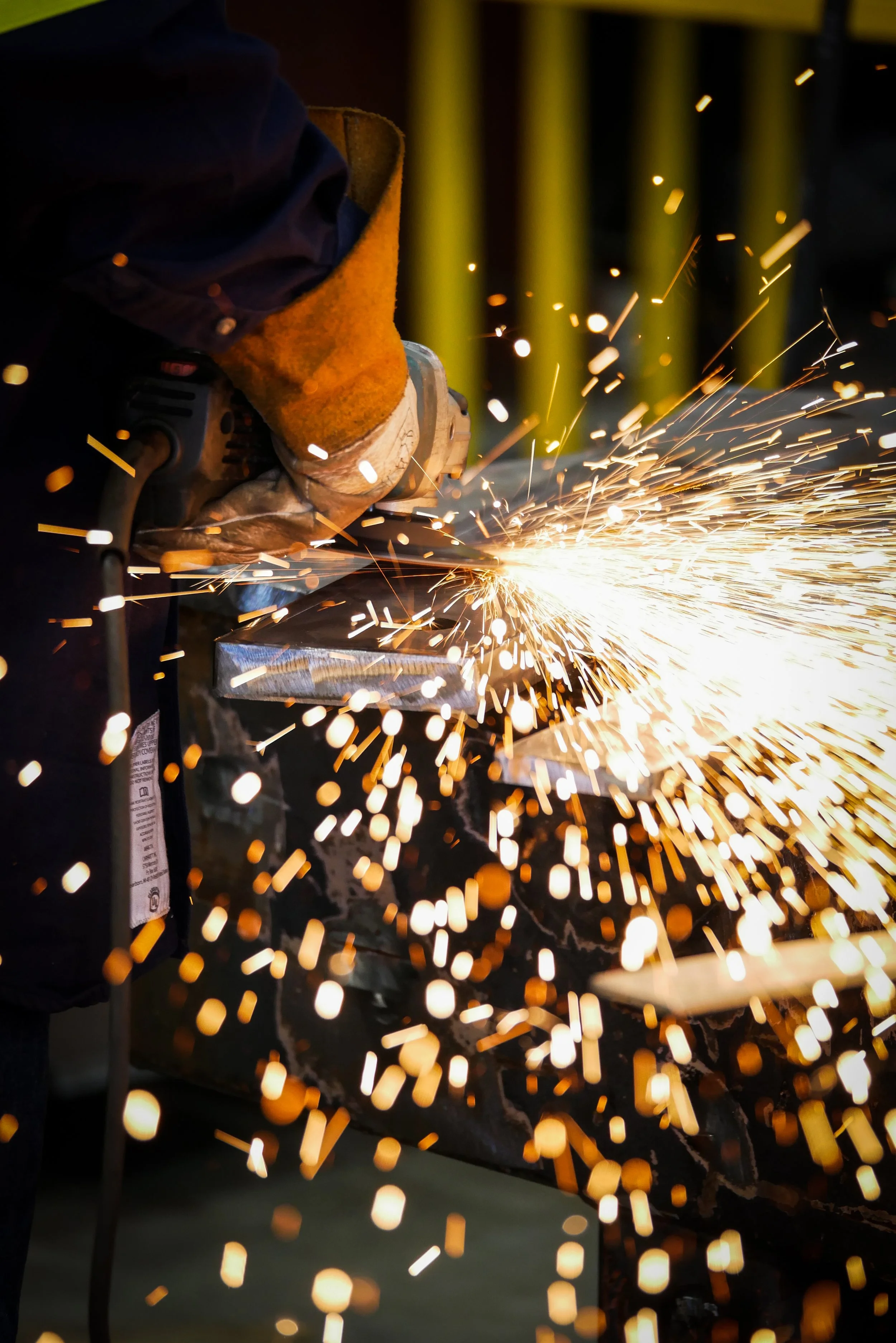 A person wearing gloves and work clothes welding metal, producing sparks.