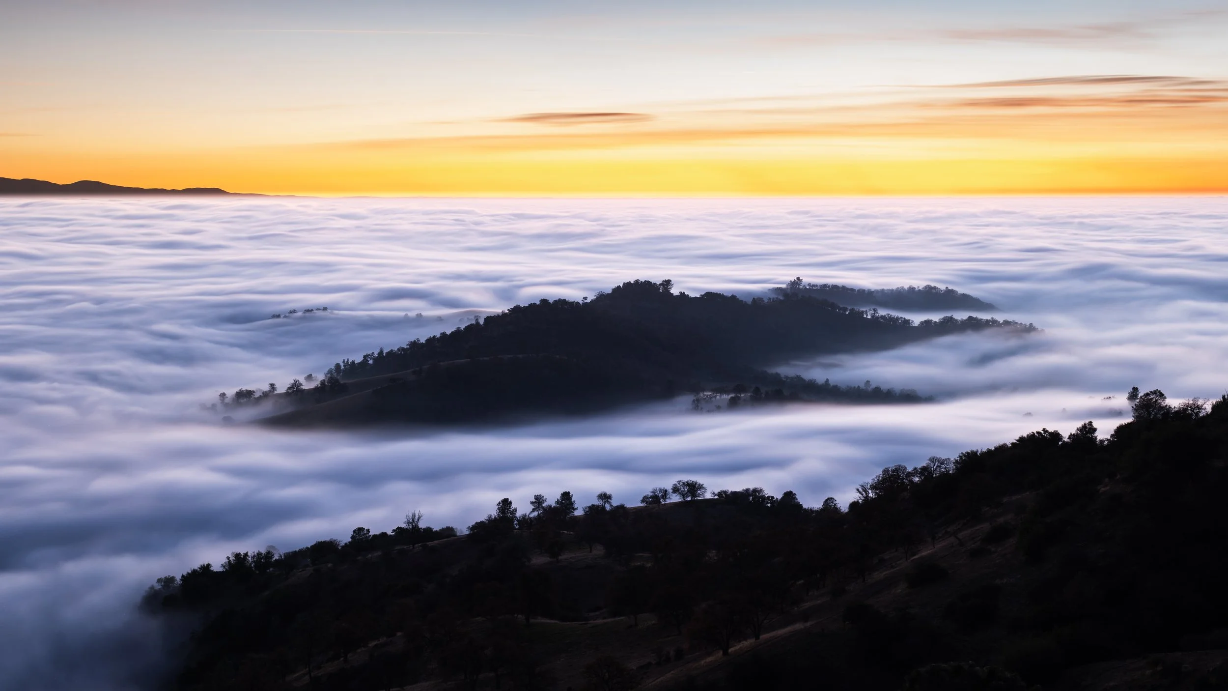 Sunset over rolling hills with a thick blanket of fog covering the valleys in between.