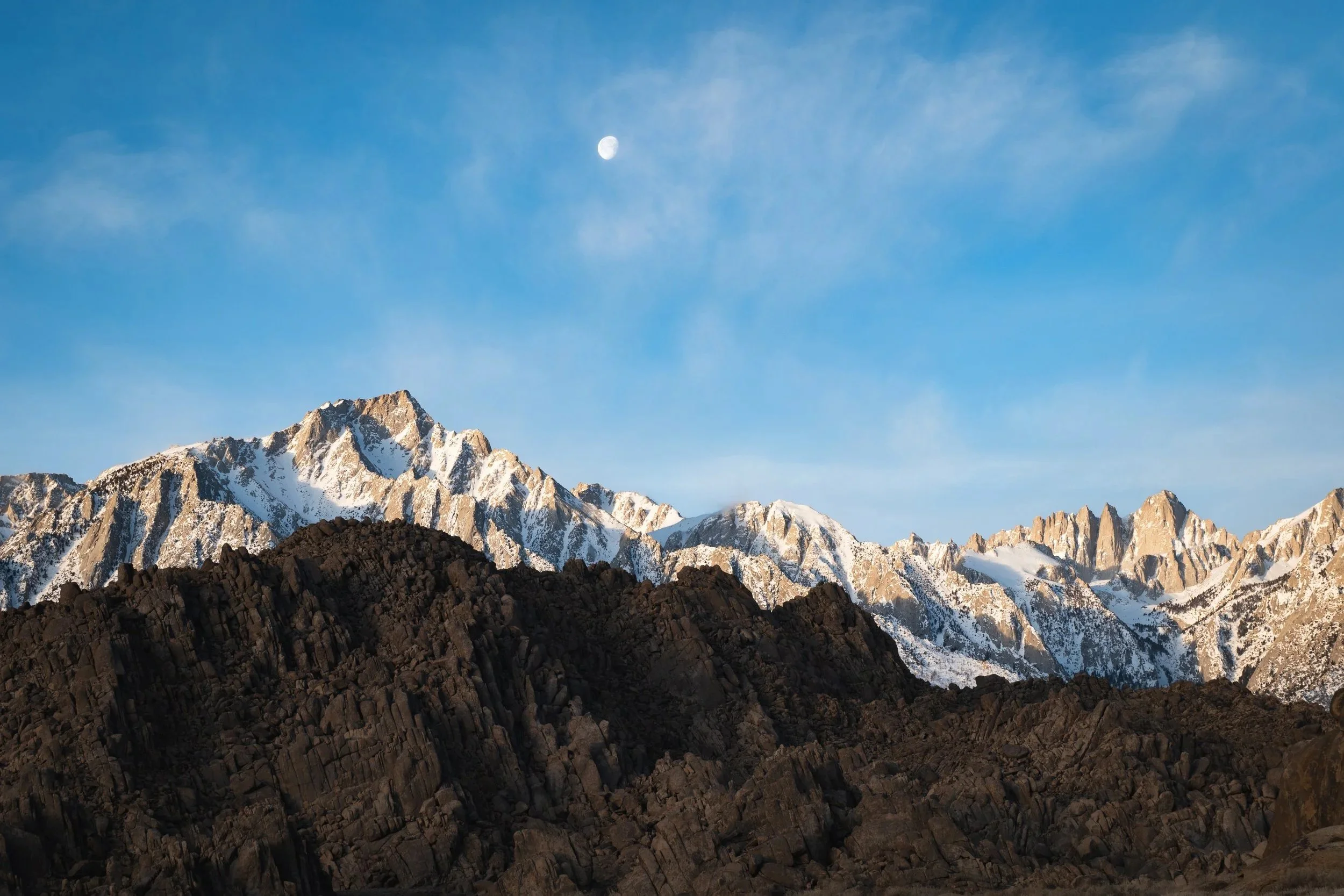 Snow-capped mountain range against a blue sky with the moon visible.