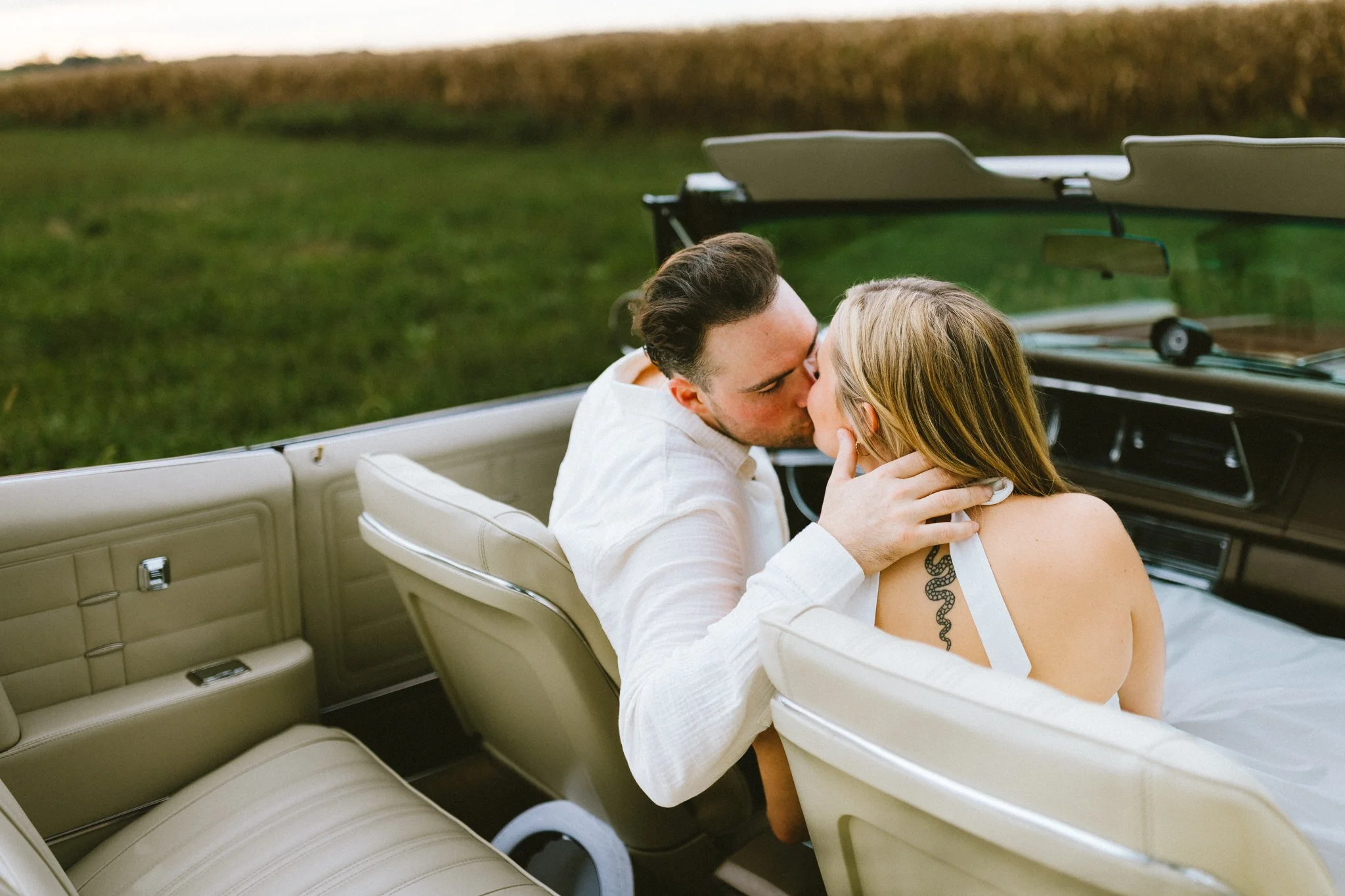Couple sharing a kiss in a vintage convertible car during engagement session